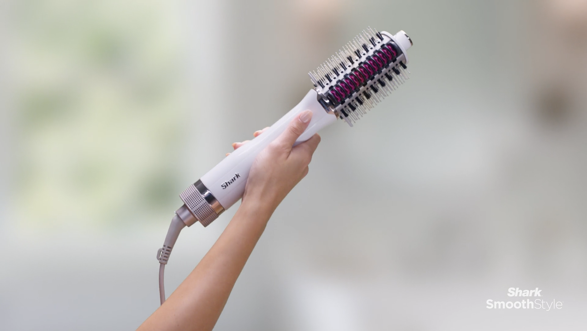 A person holding a Shark brand hair styling tool with a round brush attachment.