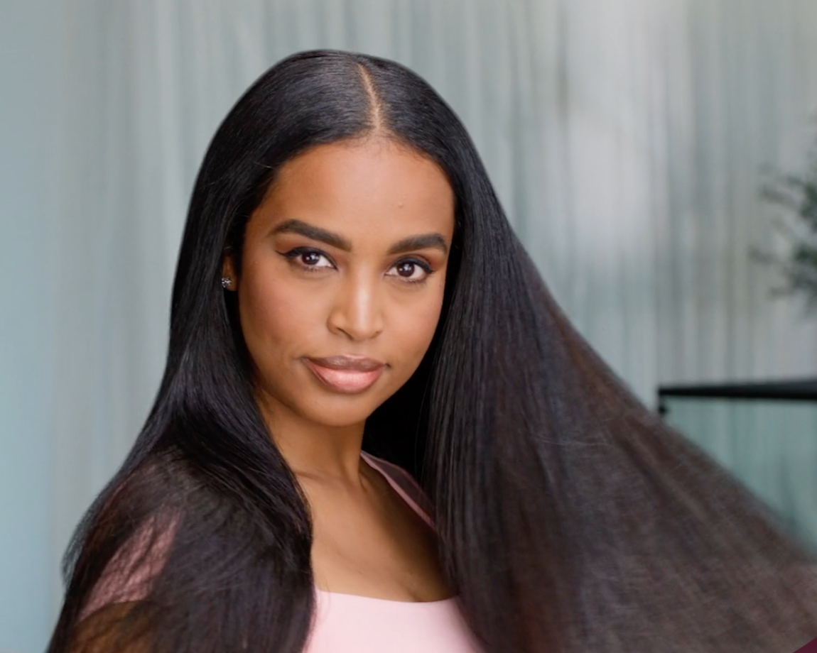 Young woman with long, straight black hair and subtle makeup, looking at the camera in an indoor setting with soft lighting