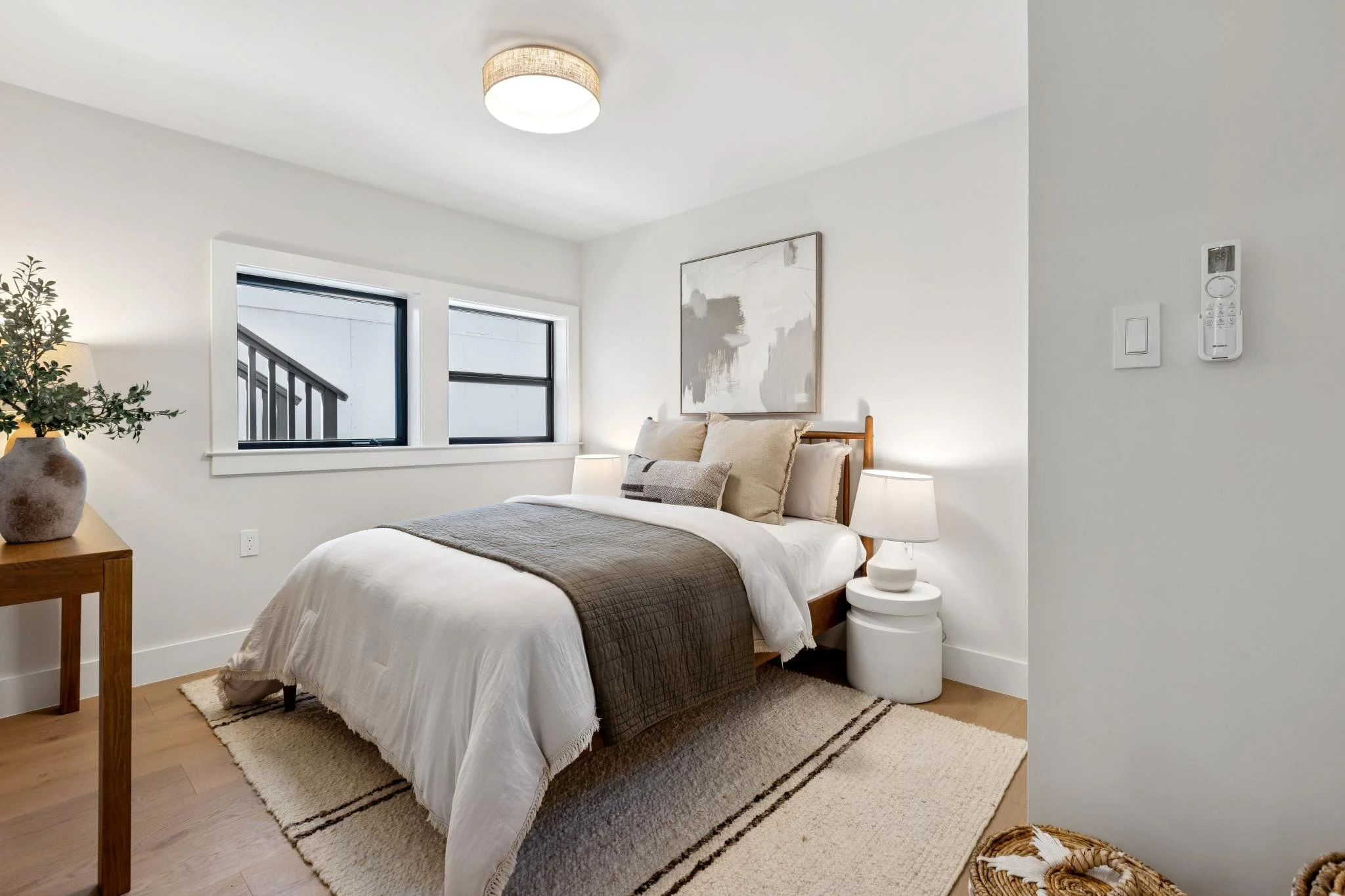 A bedroom with a bed, nightstand, and window, decorated in neutral tones and minimalist style.