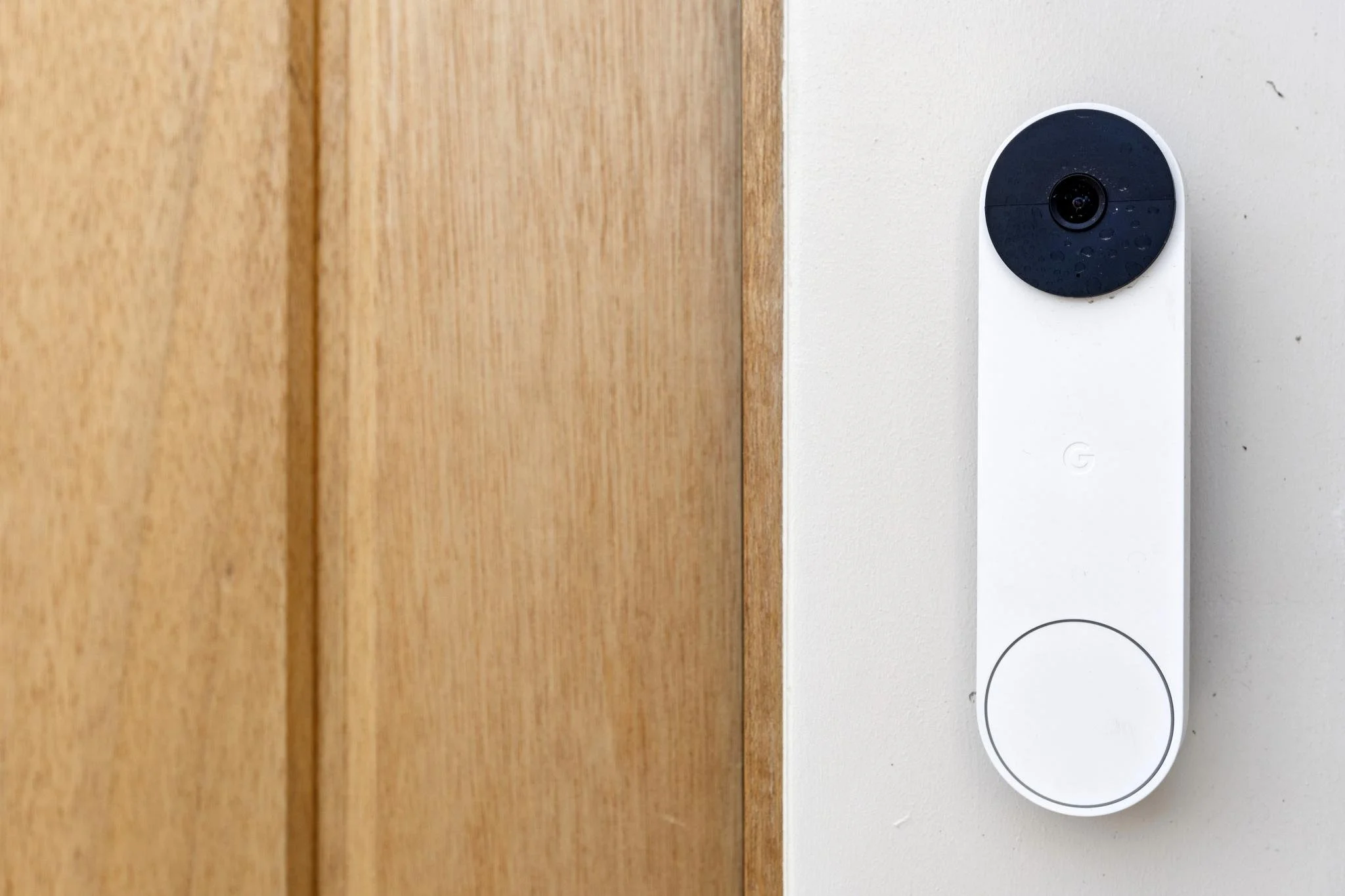 A smart thermostat on a white wall next to a wooden door frame.