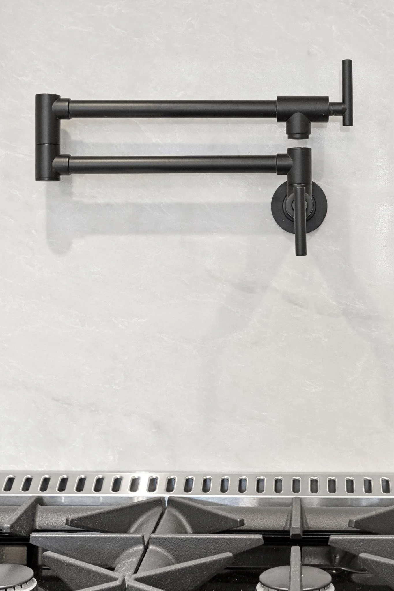 Close-up of a modern black stove with a gray speckled quartz countertop and a metal backsplash.