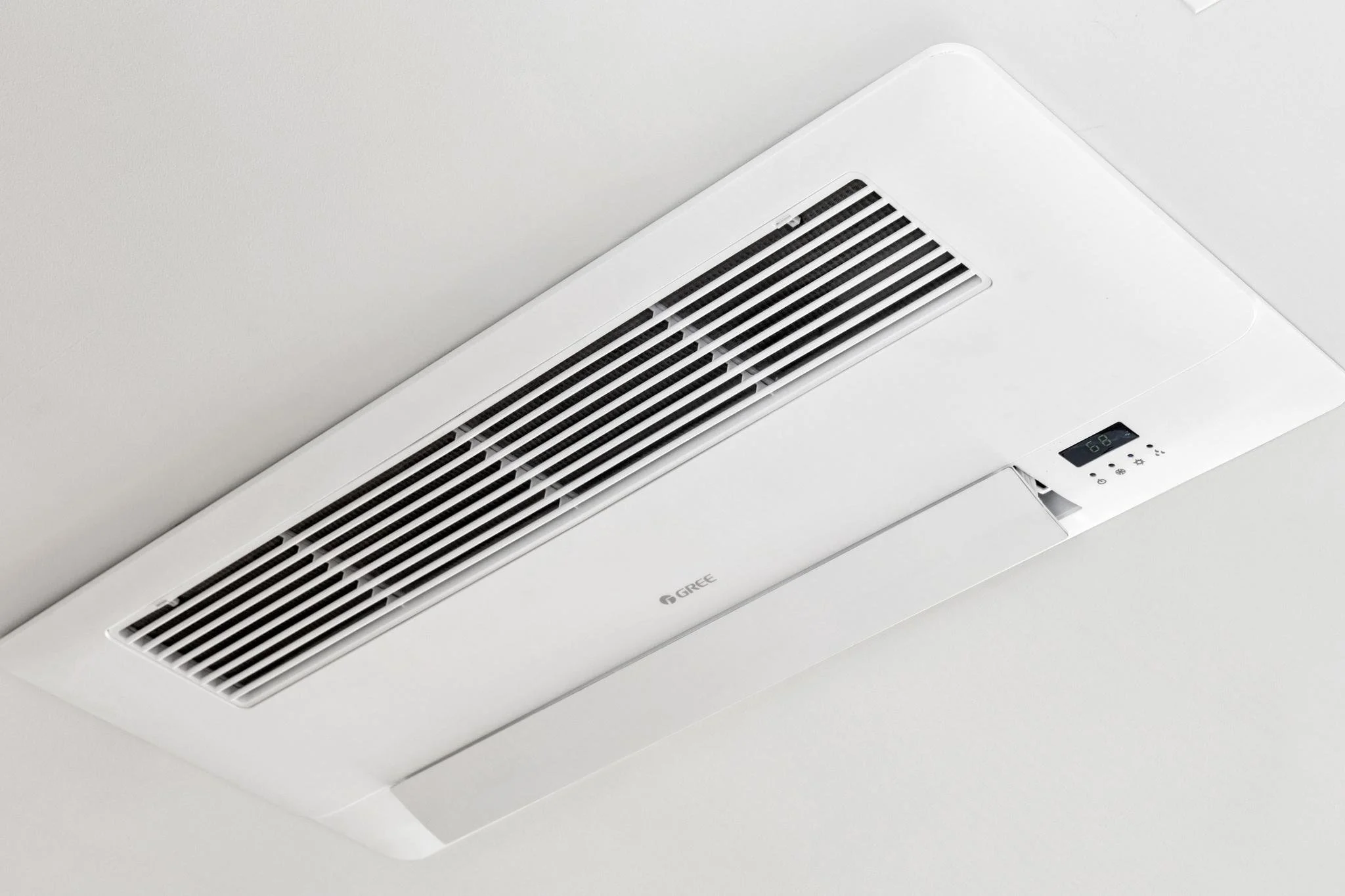 White ceiling-mounted air conditioning unit with a digital display and adjustable vents.