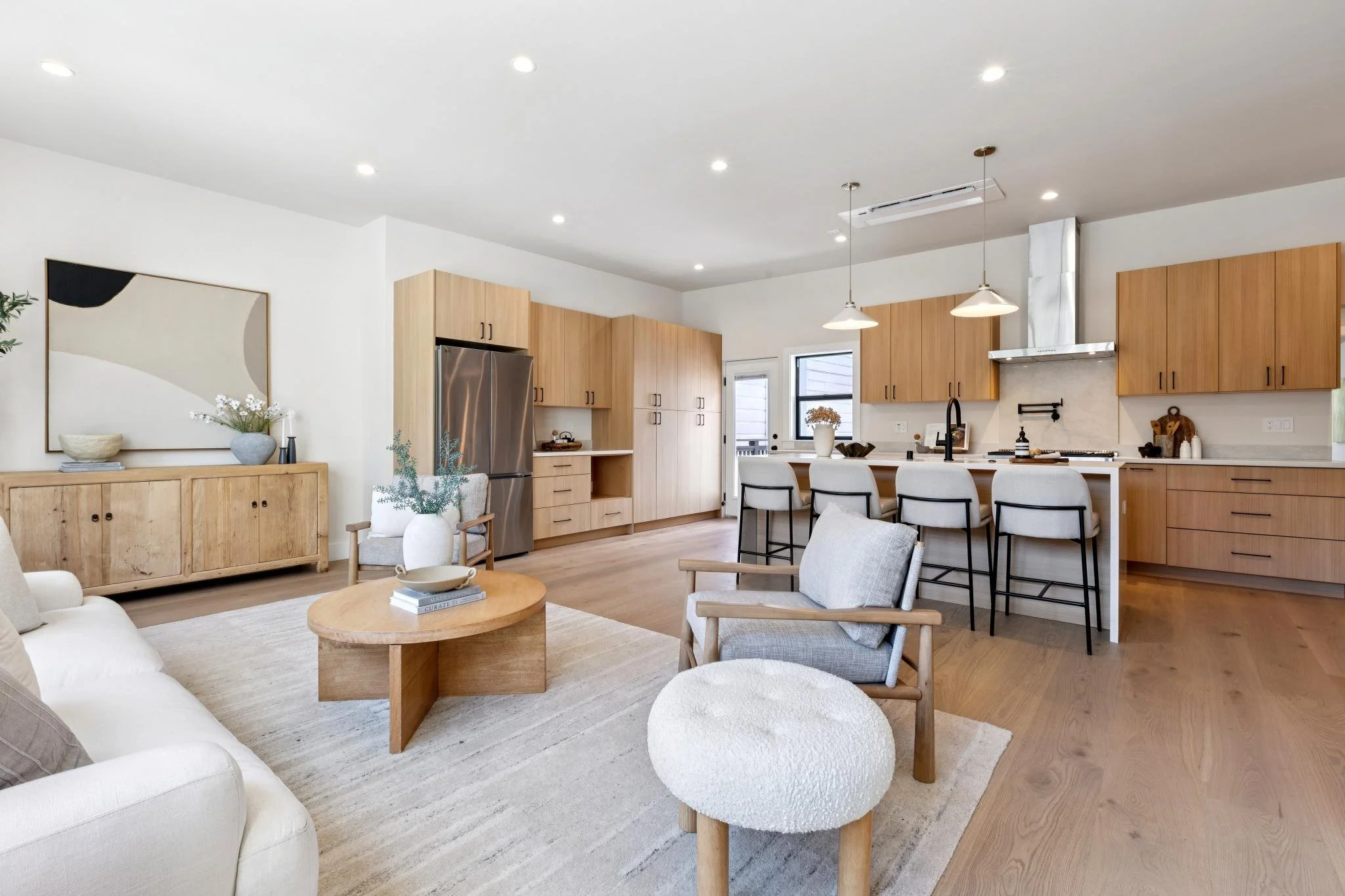 Open-concept living room and kitchen with wood cabinetry, white walls, and modern decor.