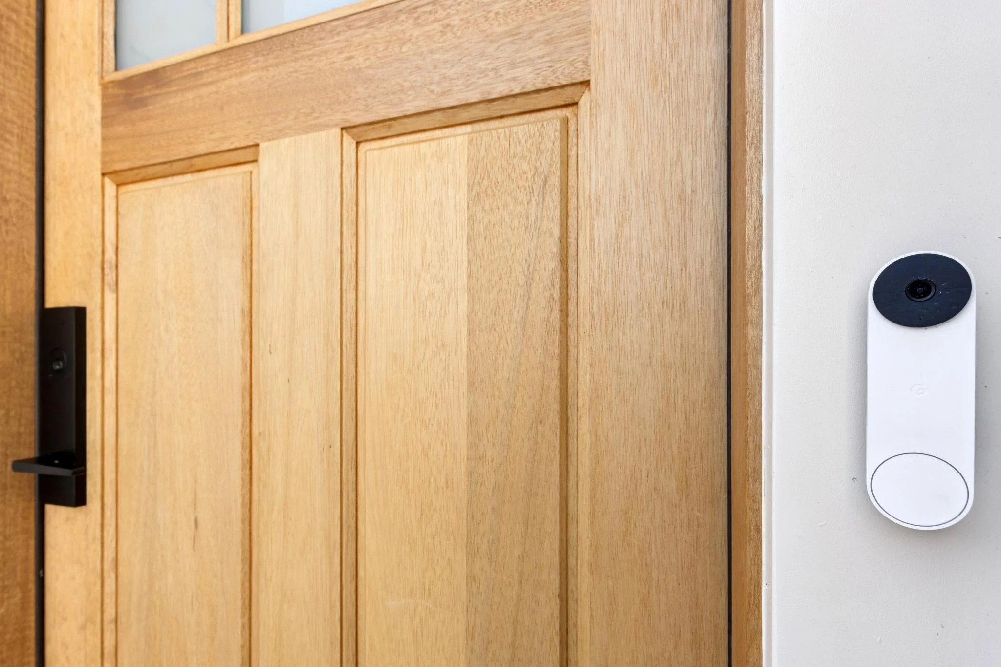Close-up of a wooden door with a black door handle and a white wall with a security camera mounted on it.