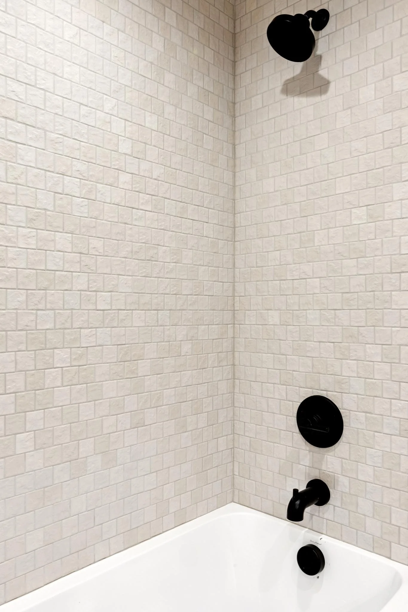 Bathroom shower with white brick-patterned tiles, black showerhead, and black fixtures.