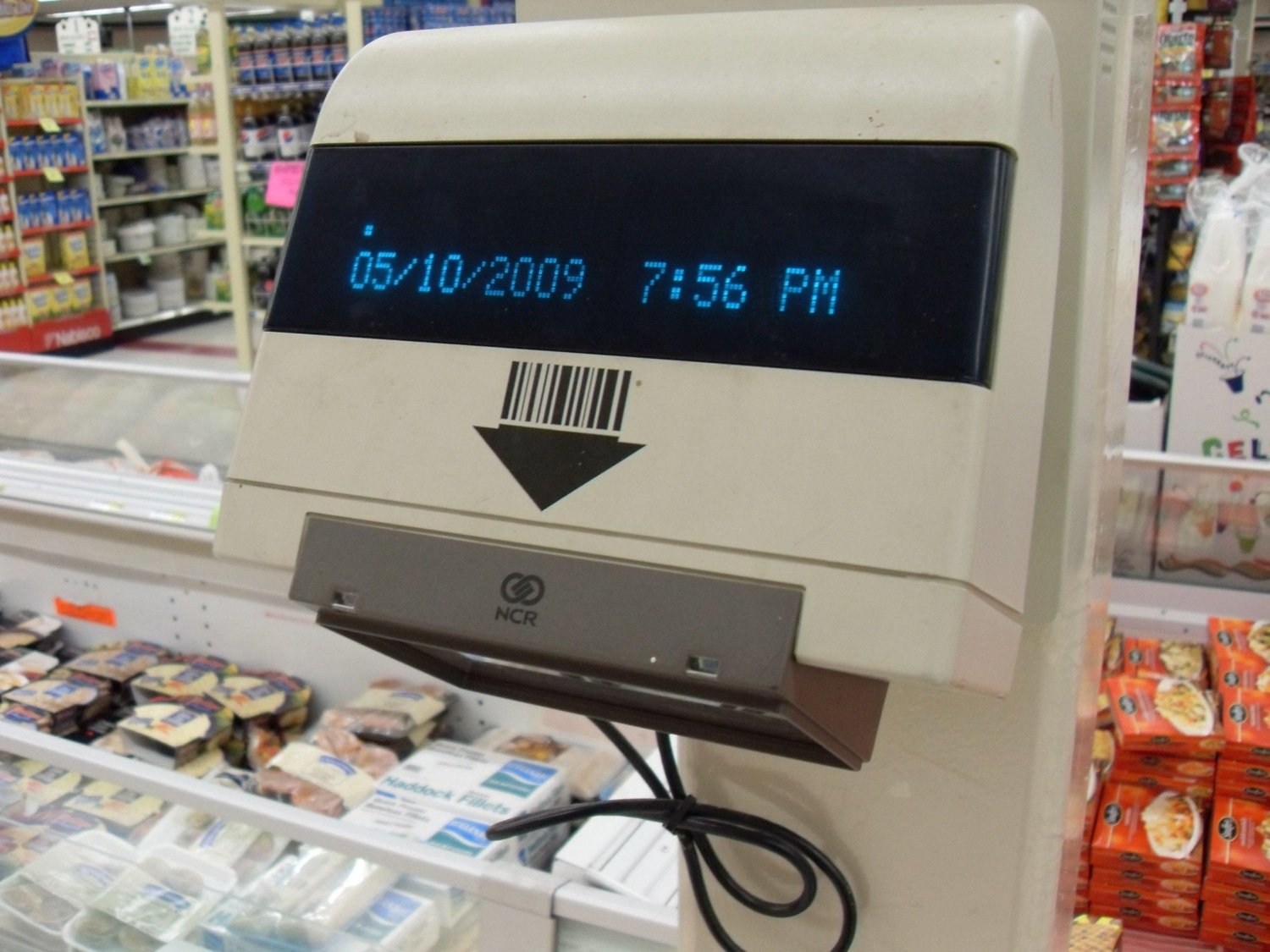 Cream-colored NCR supermarket price checker with a display above a dark scanning window and a printed barcode symbol.