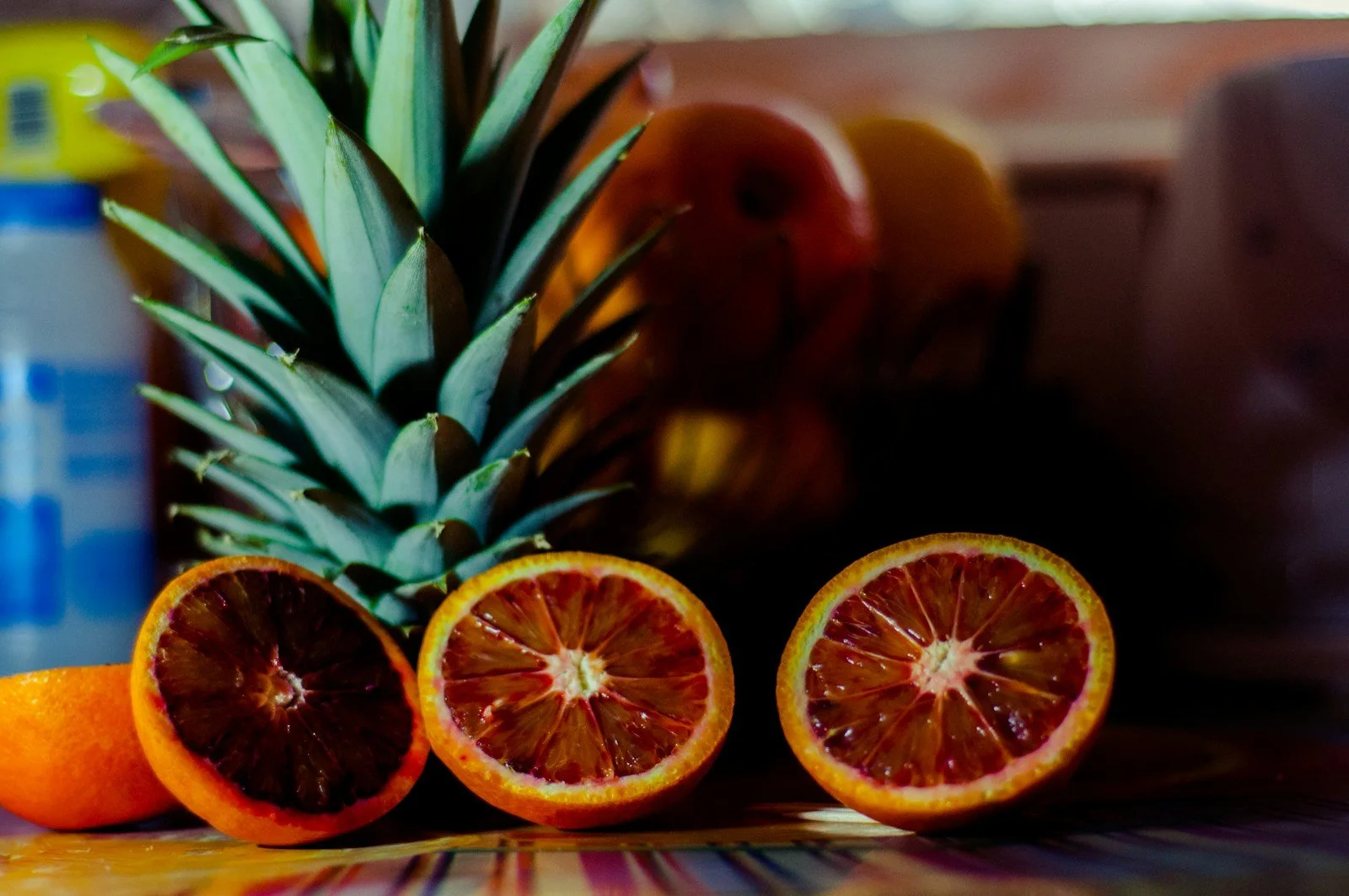 Cut red-fleshed oranges in the foreground, with pineapple leaves and whole fruit behind them.