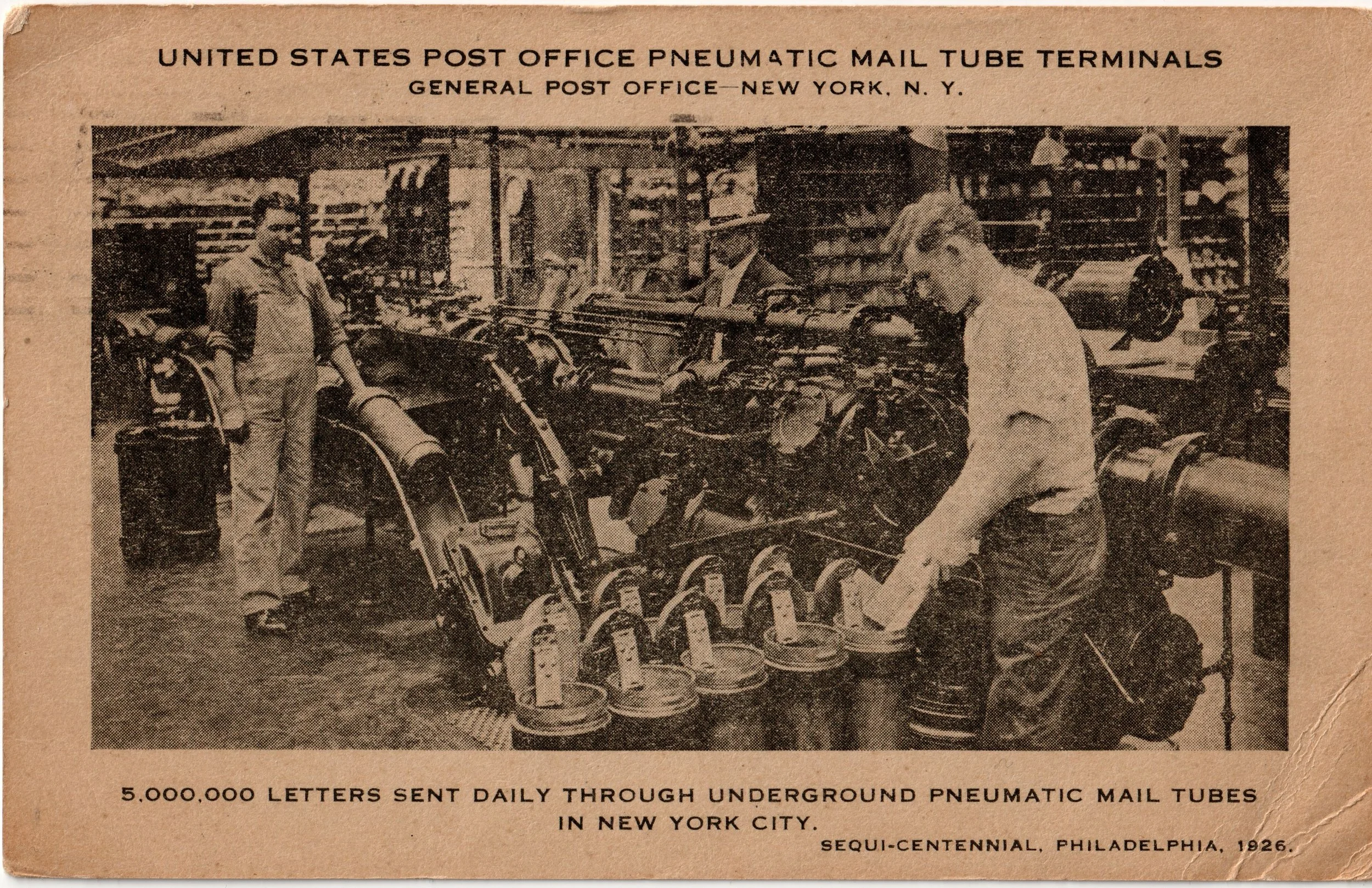 Sepia postcard showing three postal workers beside pneumatic mail tubes and rows of cylindrical mail carriers in New York.