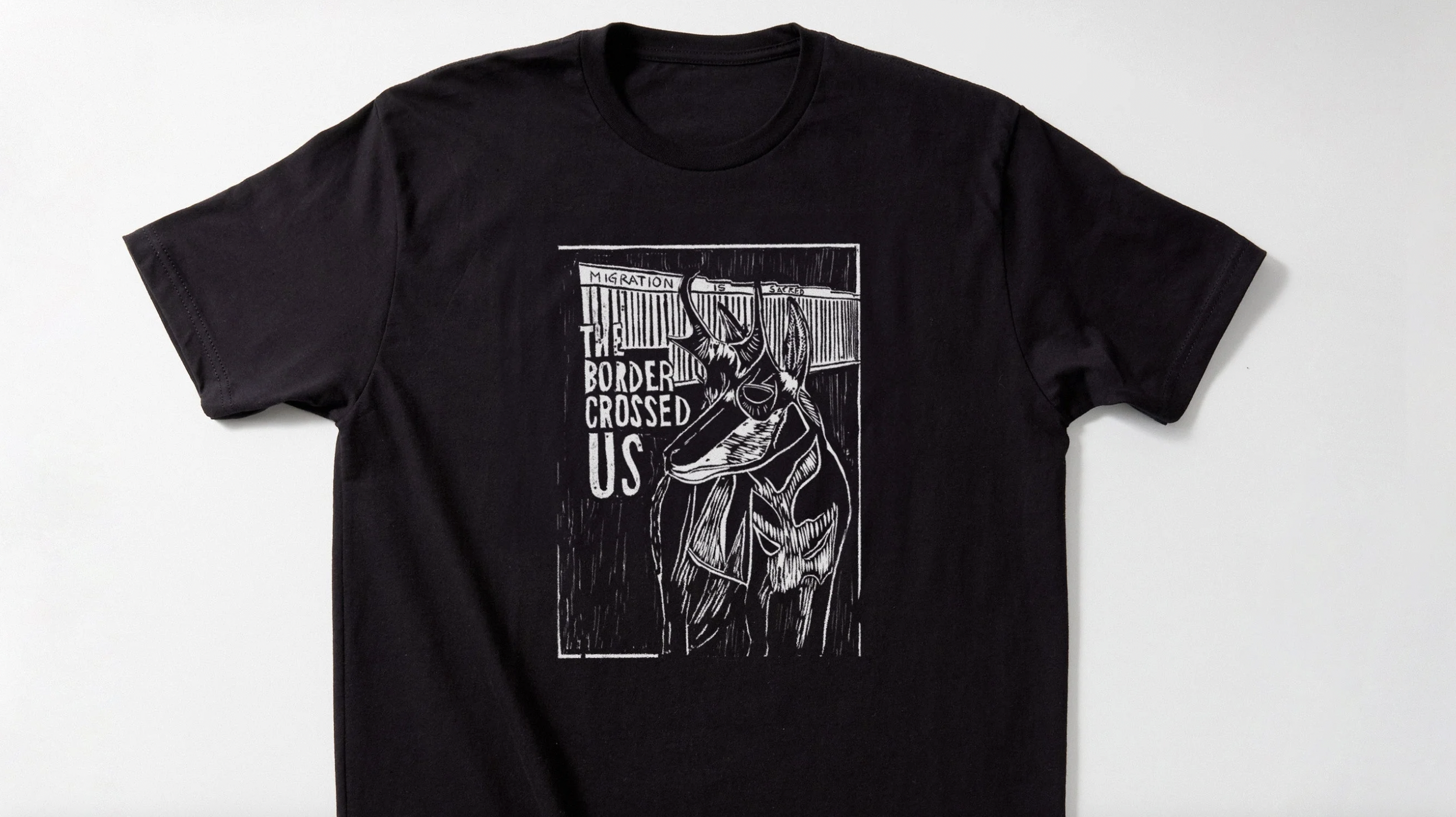 Black t-shirt with a graphic design featuring a human heart and the words "Migration is sacred, the border crossed us".
