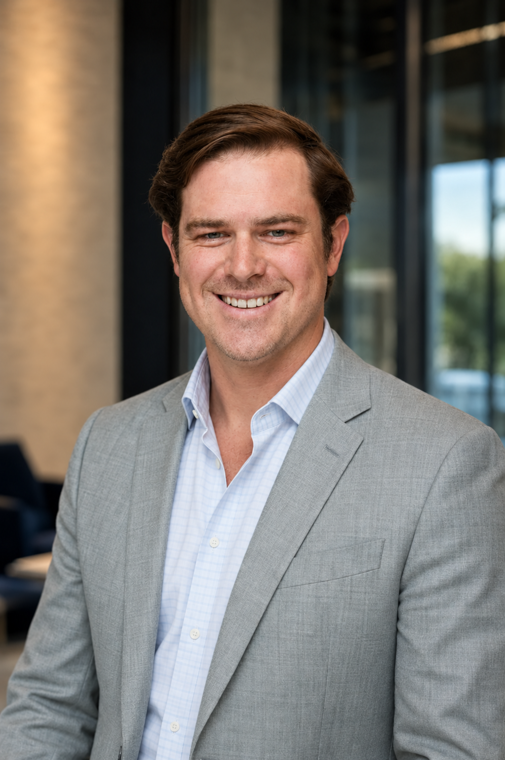 Professional man in a light gray suit smiling in an office environment.