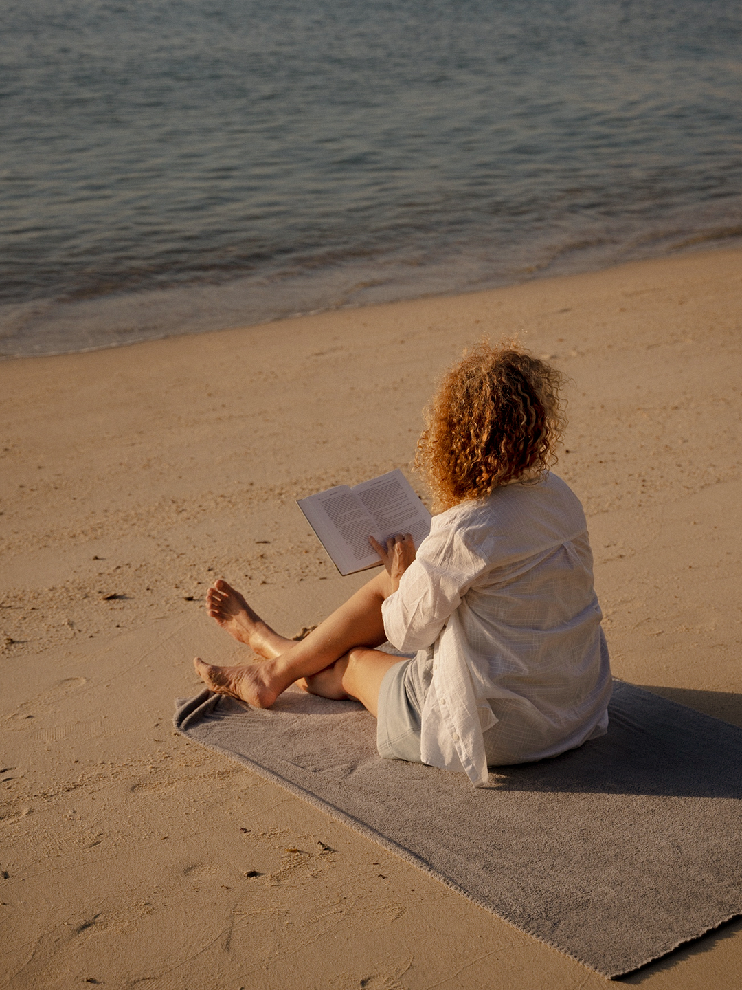 Persona leyendo un libro en la orilla de la playa durante el atardecer.