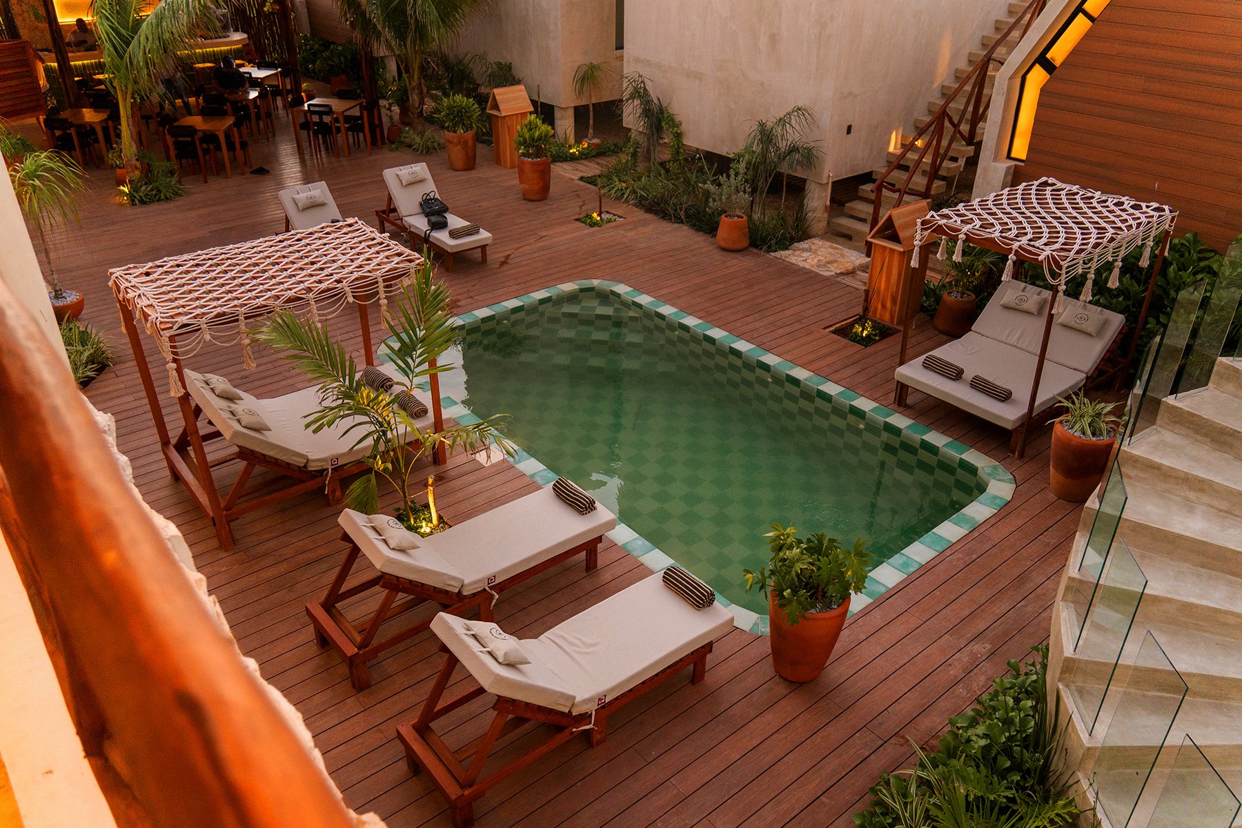 Vista de la alberca y mobiliario en una terraza con plantas decorativas y áreas de descanso en un entorno de hotel.