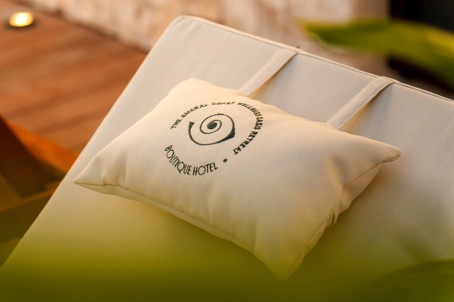 Almohada con logotipo del hotel y las palabras 'The Emerald Coast Wellness Oasis Retreat Boutique Hotel', sobre una cama con ropa de cama blanca.