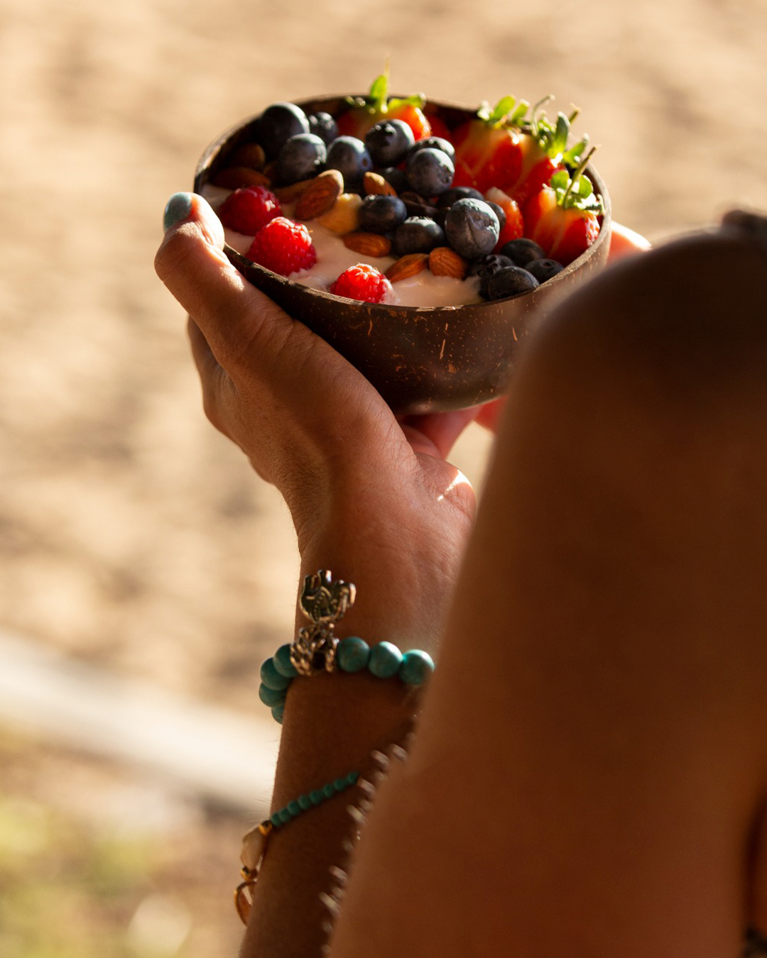 Mano sosteniendo un cuenco con yogur cubierto de bayas, almendras y fresas.