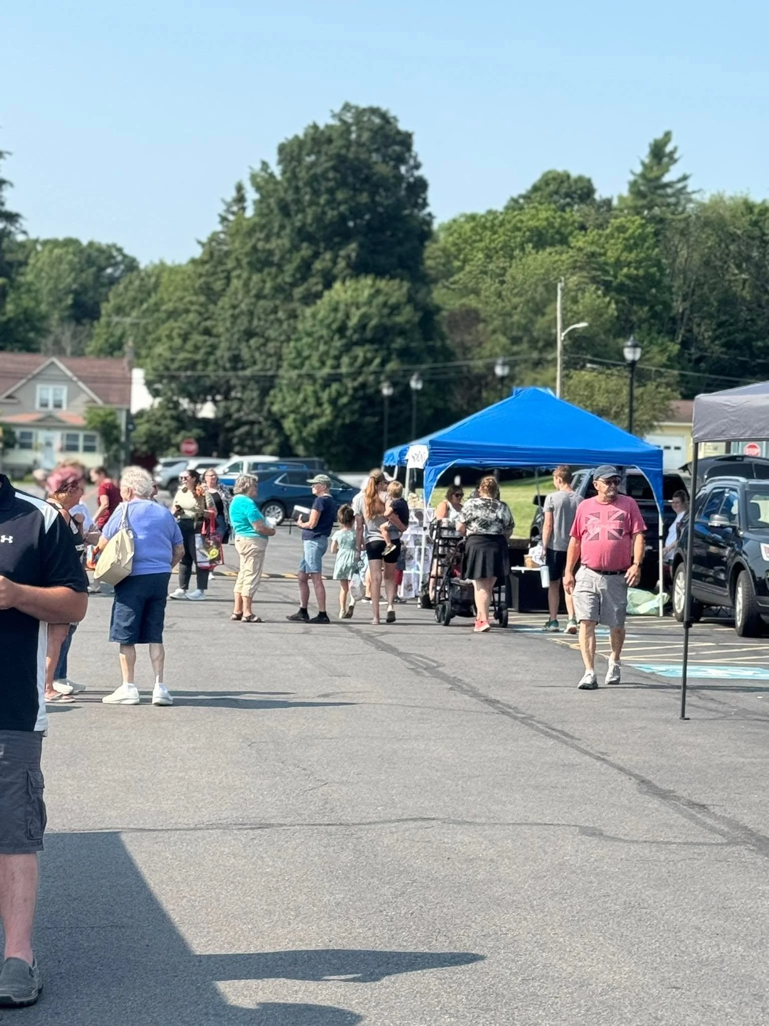People gathered outdoors at a community event with tents and trees in the background.