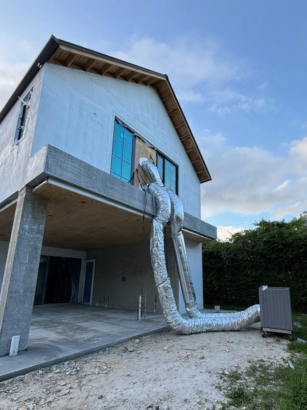 A house under construction with large silver air ducts running from the roof to the ground.