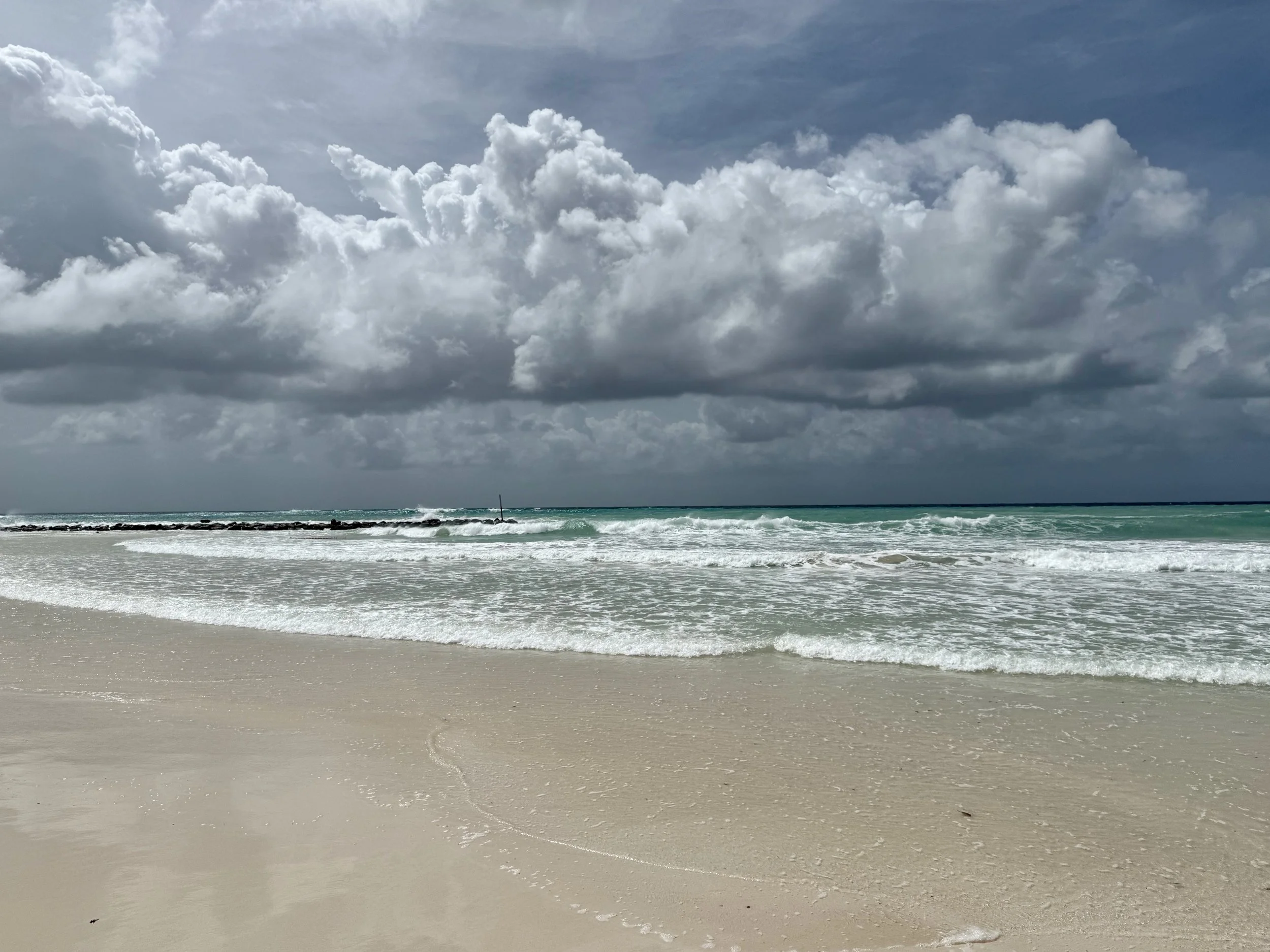 Ocean waves crashing onto a sandy beach under a cloudy sky.