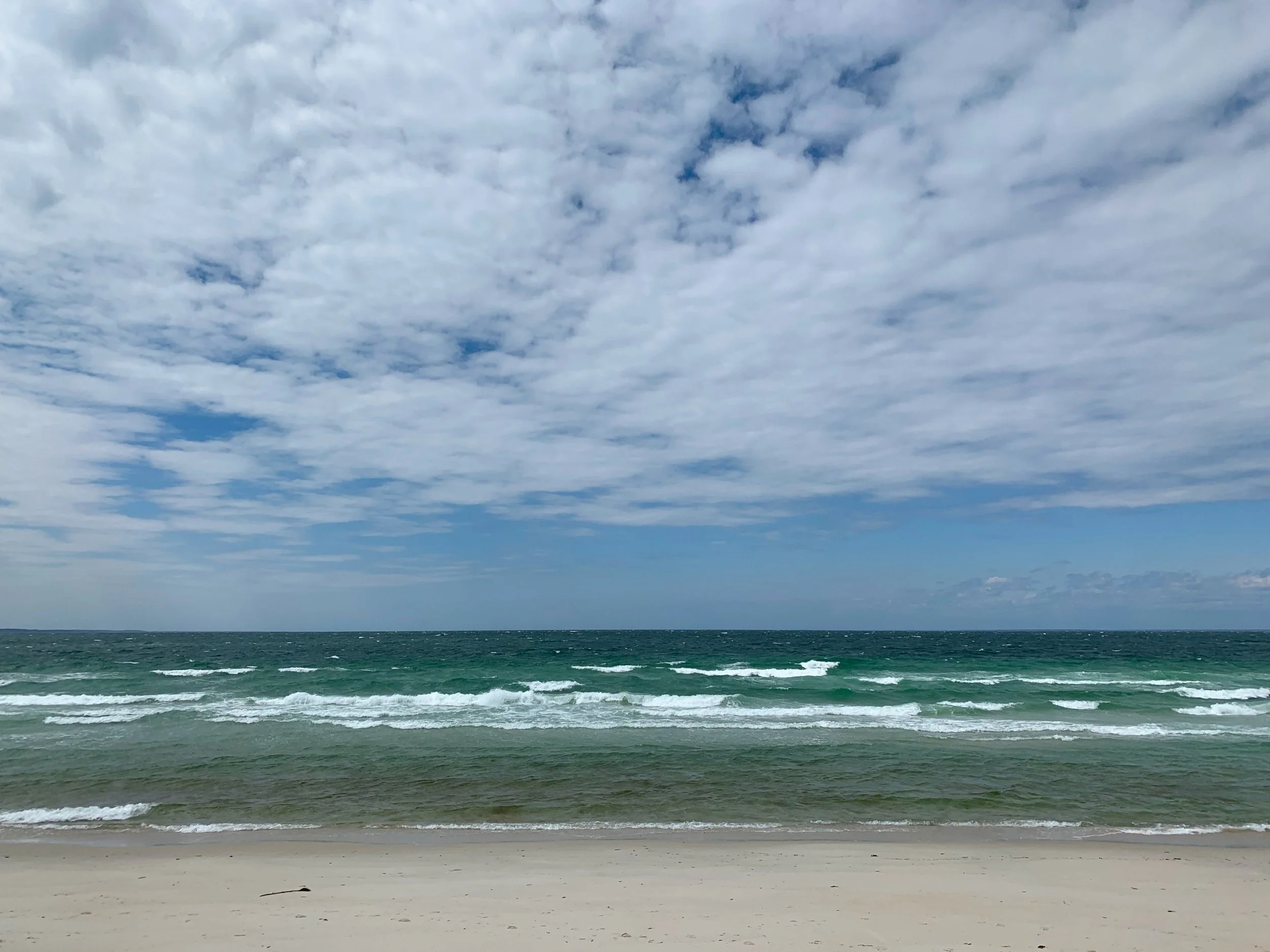 A beach with sandy shore, ocean waves, and a cloudy sky overhead.