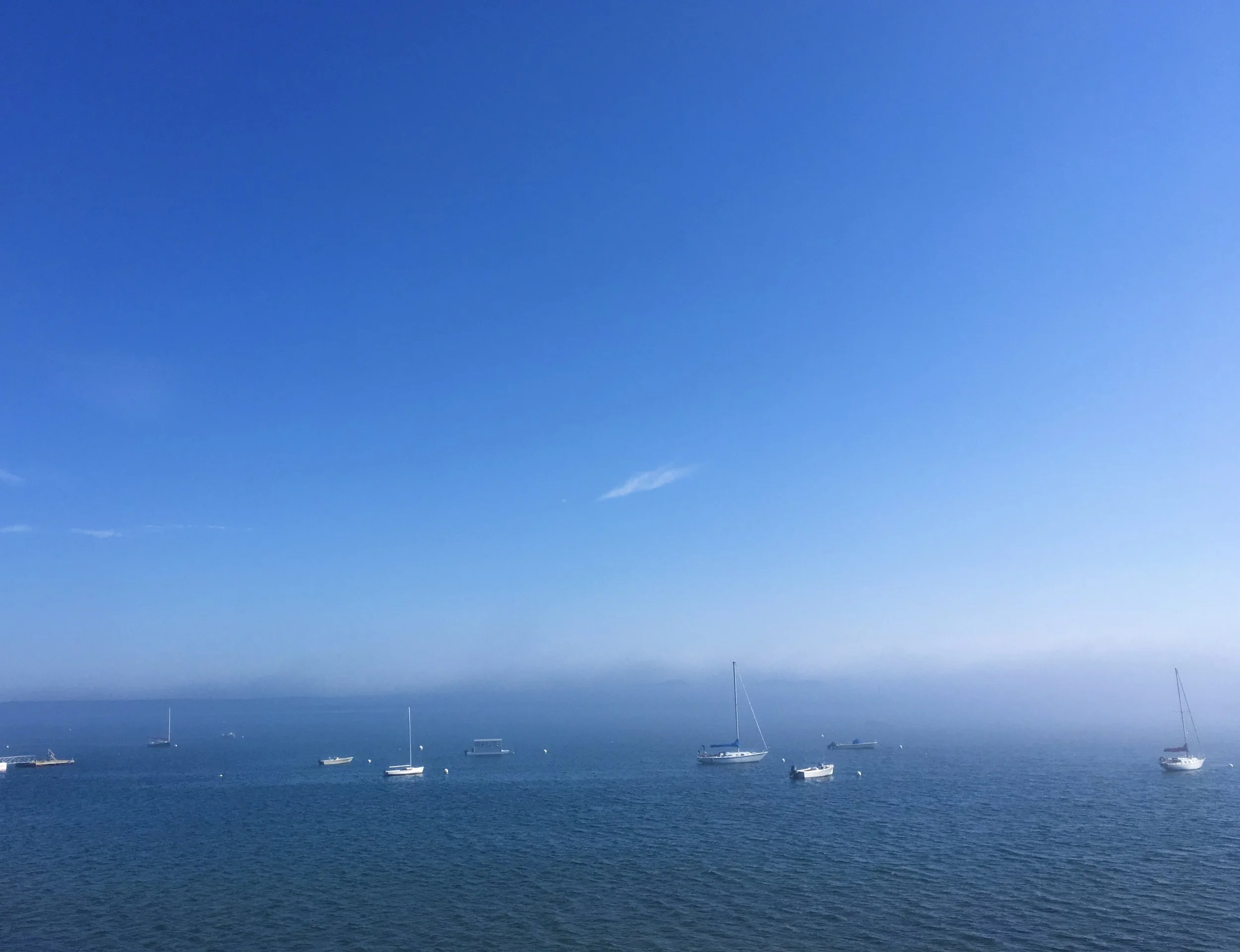 Blue sky with calm ocean waters and multiple sailboats anchored or sailing in the distance.