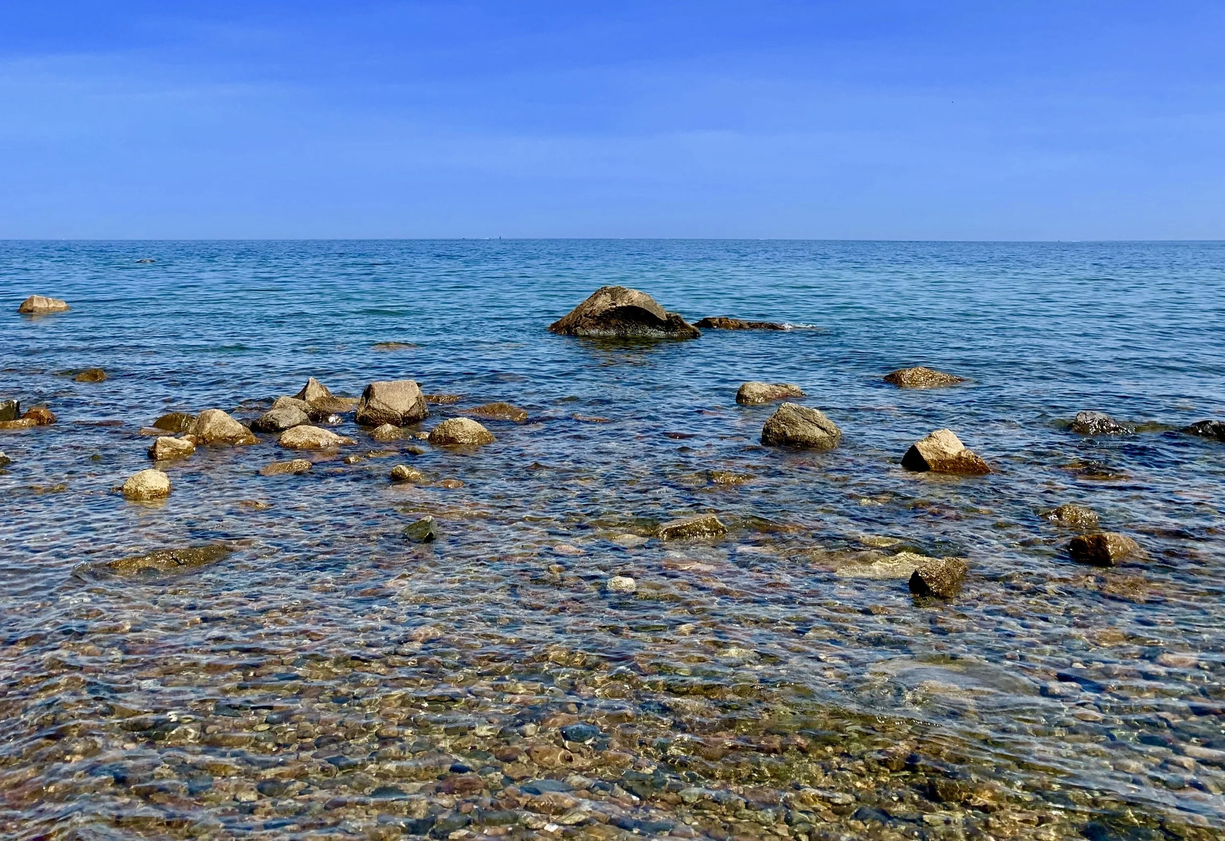 View of the ocean with a clear blue sky, showing water and rocks along the shoreline.