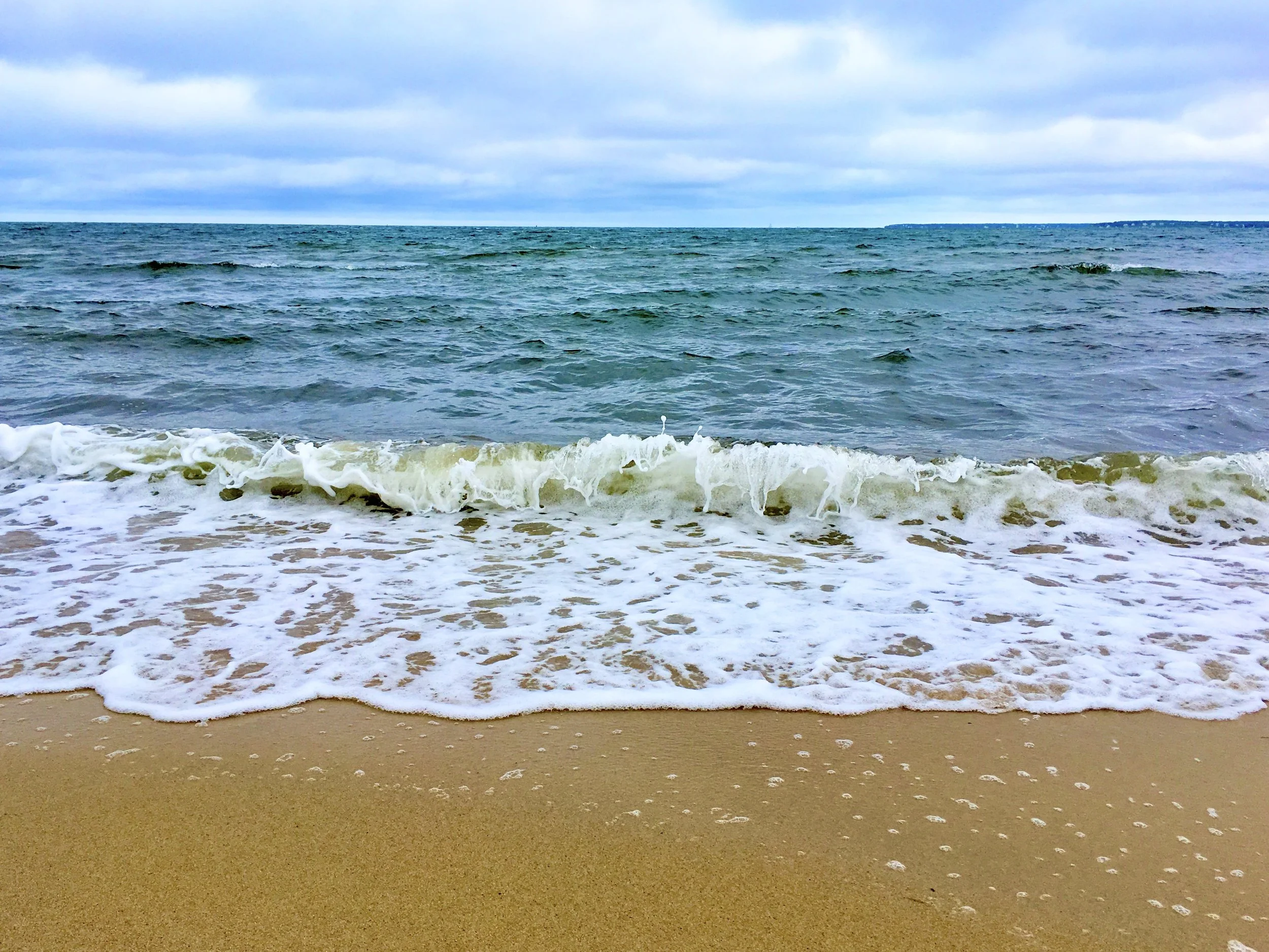 Beach with sandy shoreline, small waves, and a cloudy sky.
