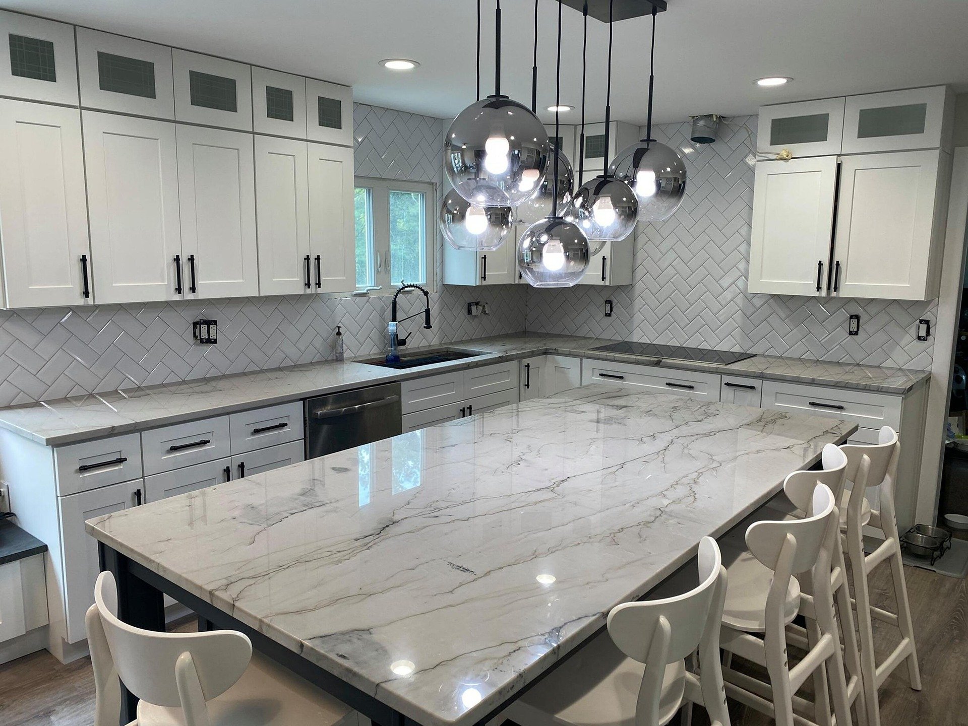 Modern kitchen remodeling in Frisco, Texas with white cabinets, herringbone tile backsplash, marble countertops, black hardware, and pendant lighting over a kitchen island.