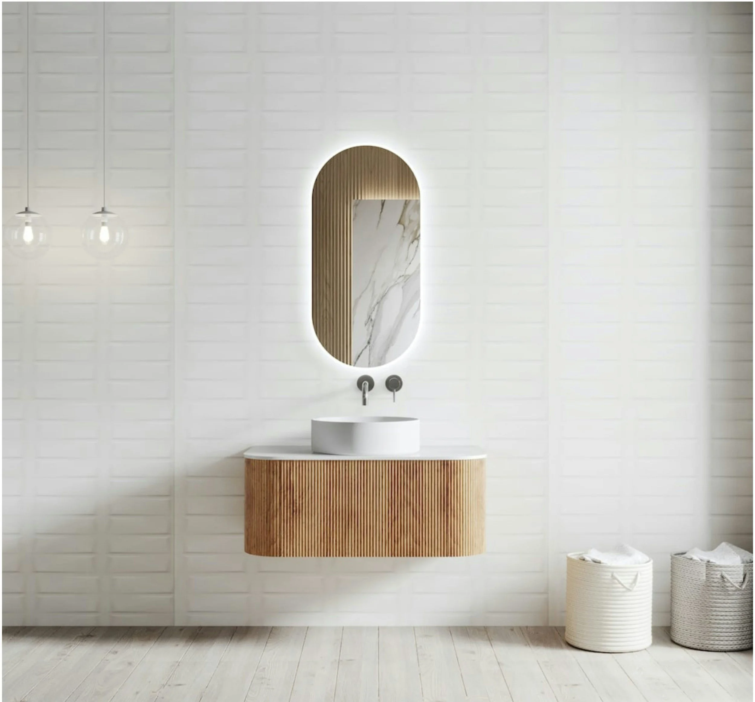 A modern bathroom with a large, round mirror backlit with LED lighting, a minimalist white sink, light-colored wooden accents, and white tiled walls with horizontal wooden slat detail around the mirror. There are two pendant lights hanging on the left side of the image and a basket with rolled towels on the right.