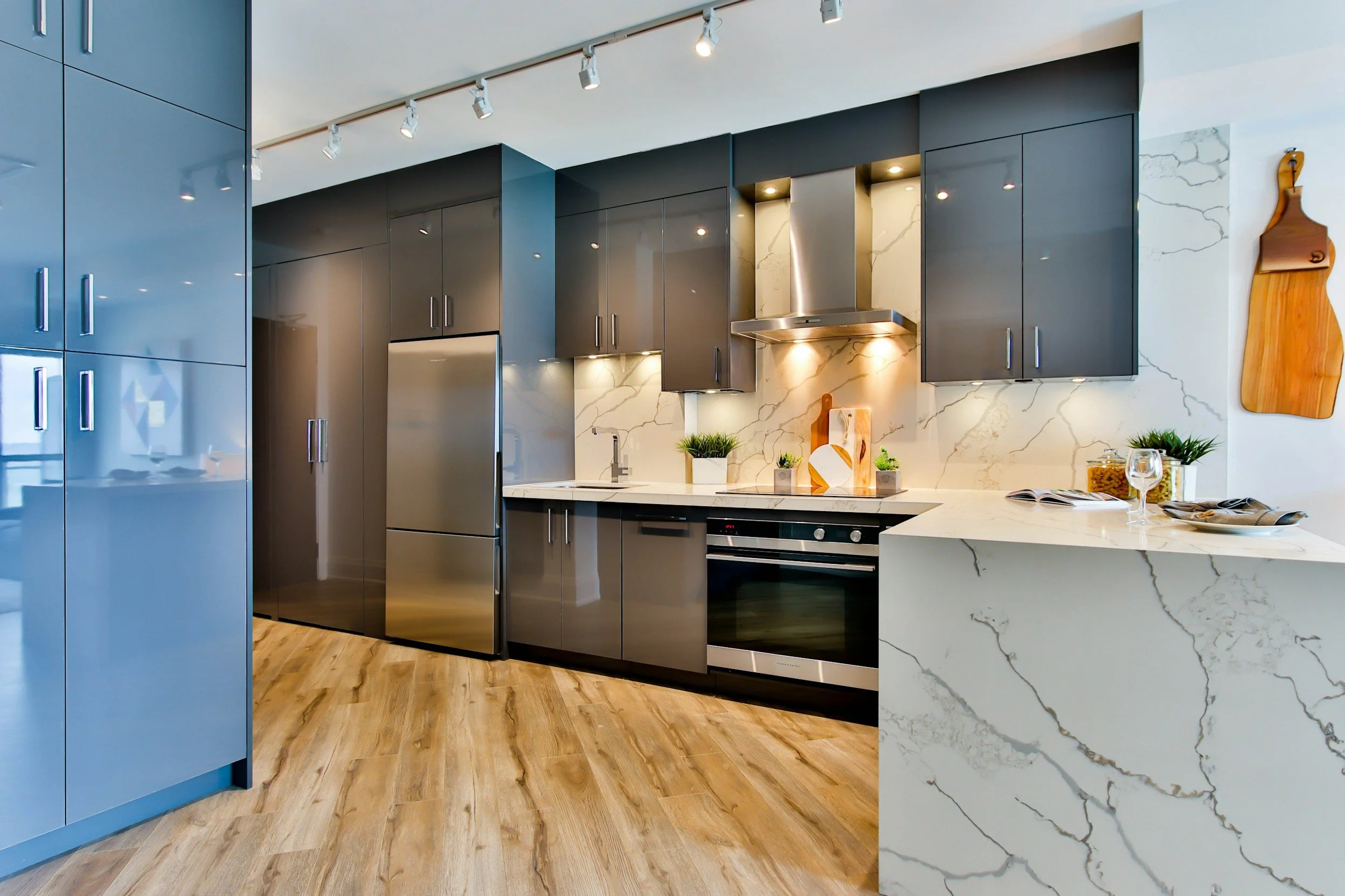 Modern kitchen with blue and black cabinets, marble backsplash, stainless steel appliances, wooden flooring, and decorative plants on the counter.