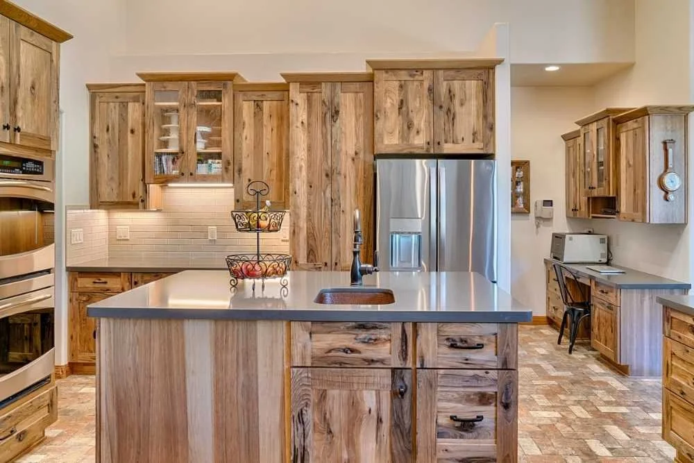 Kitchen remodel in Dallas, Texas with wooden cabinets, stainless steel refrigerator, island with a sink, and small workspace with a microwave and chair.