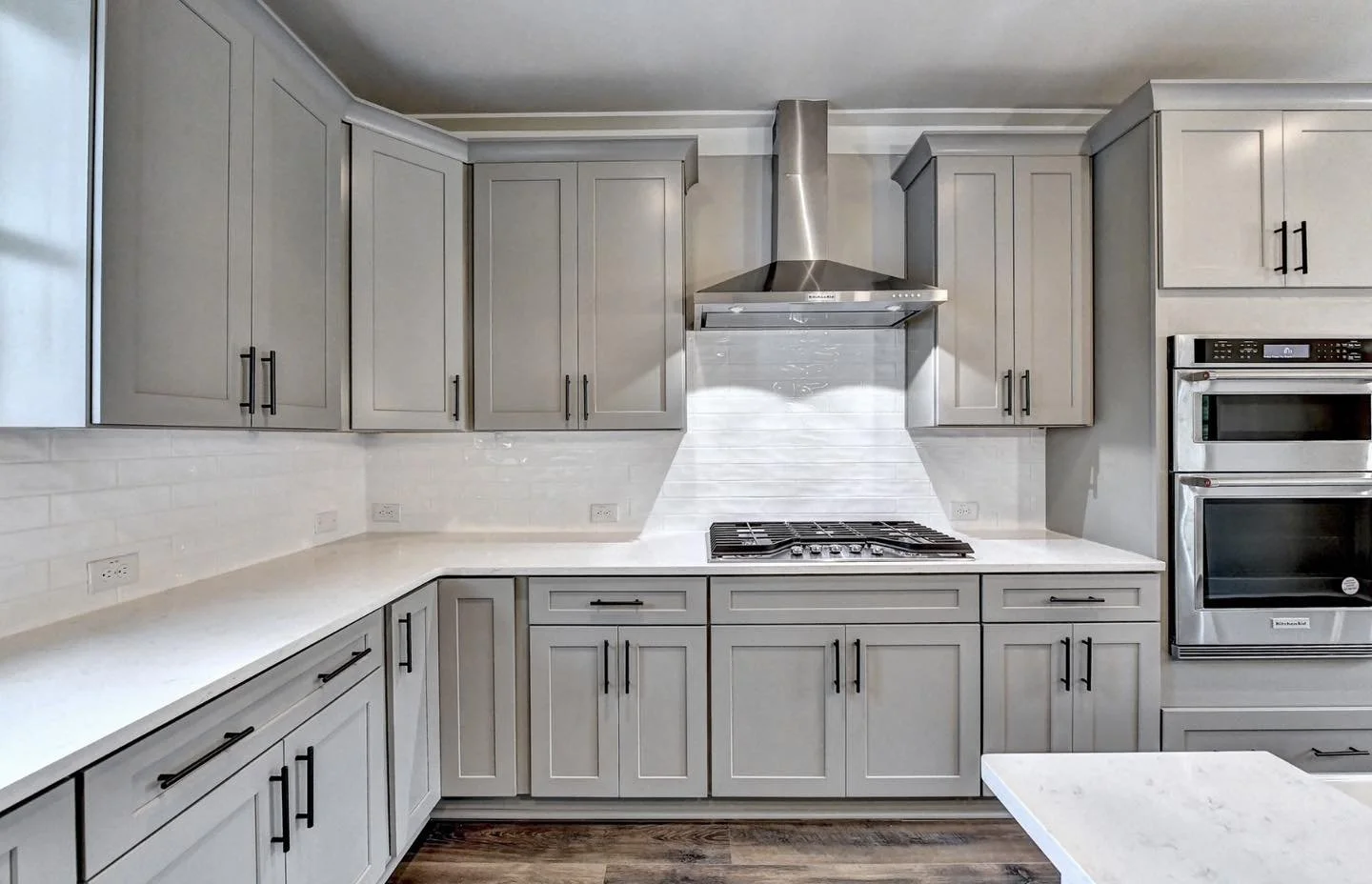Kitchen remodeling project in McKinney, Texas. Gray cabinets, stainless steel range hood, white tile backsplash, built-in stainless steel microwave, and gas stove on white countertop.