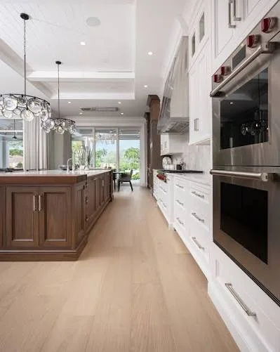 Modern kitchen with a large island, white cabinets, built-in oven, and a view of the backyard through sliding glass doors.