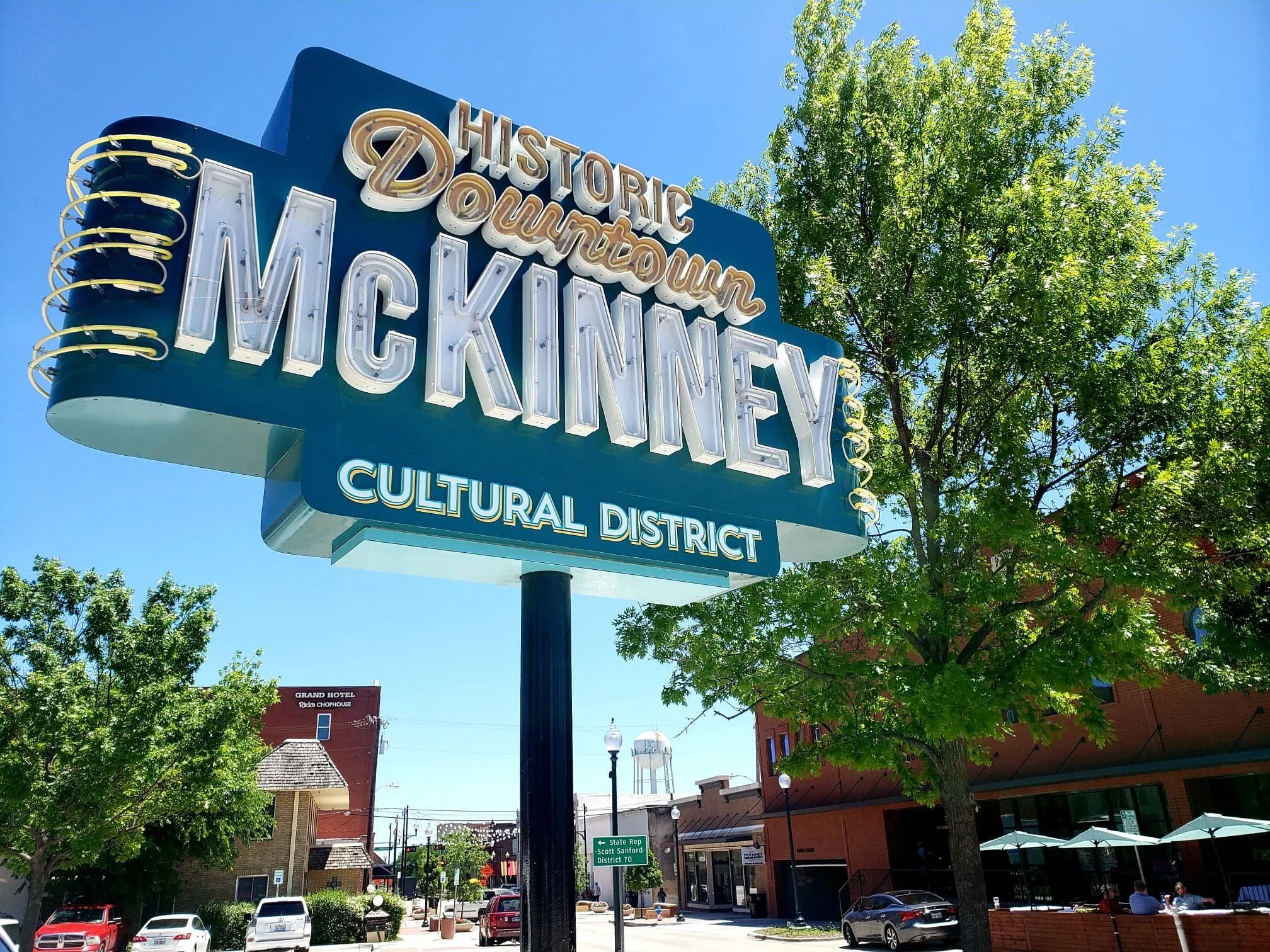Historic Downtown Mickinney sign in a small town with trees and buildings in the background.