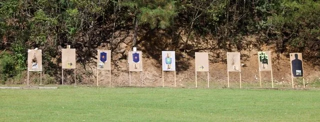 Series of shooting targets on a grassy field with trees in the background.