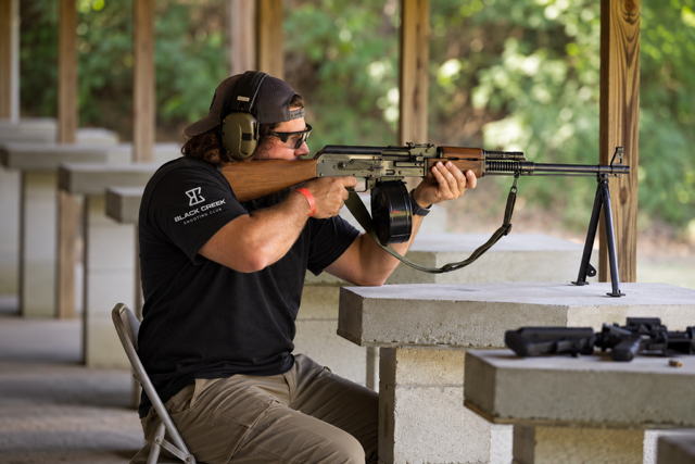 Man wearing ear protection aiming a rifle at a shooting range.