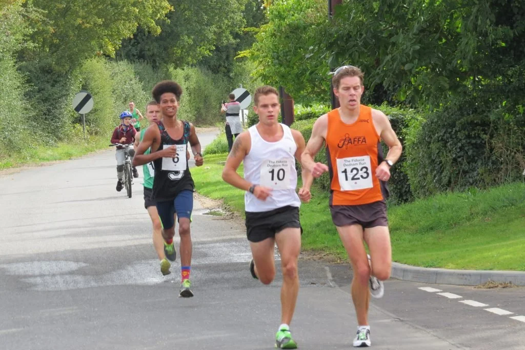 A group of runners participating in a race on a paved road with lush green trees and bushes on either side.