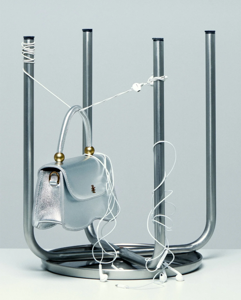 A silver handbag hanging on a metal coat rack with tangled white earphones draped over it