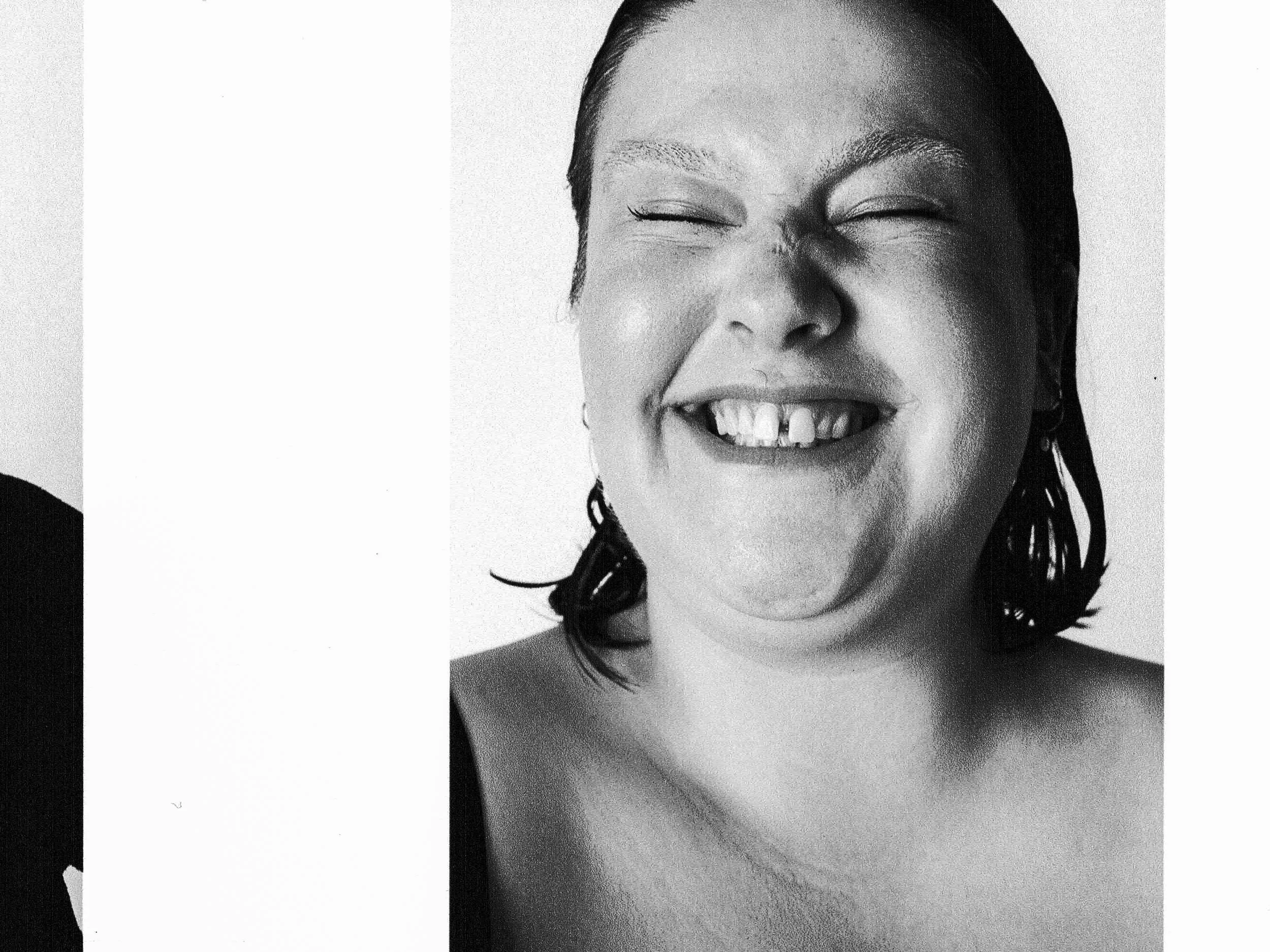 A black and white photograph of a smiling woman with closed eyes, showing her teeth, with dark hair styled back.