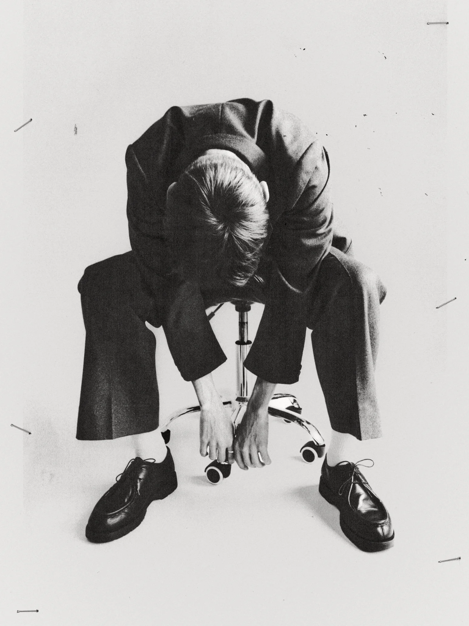 A person is sitting on a skateboard with their head bowed down, wearing a hooded jacket, with their hands on their knees, in a black-and-white photo.