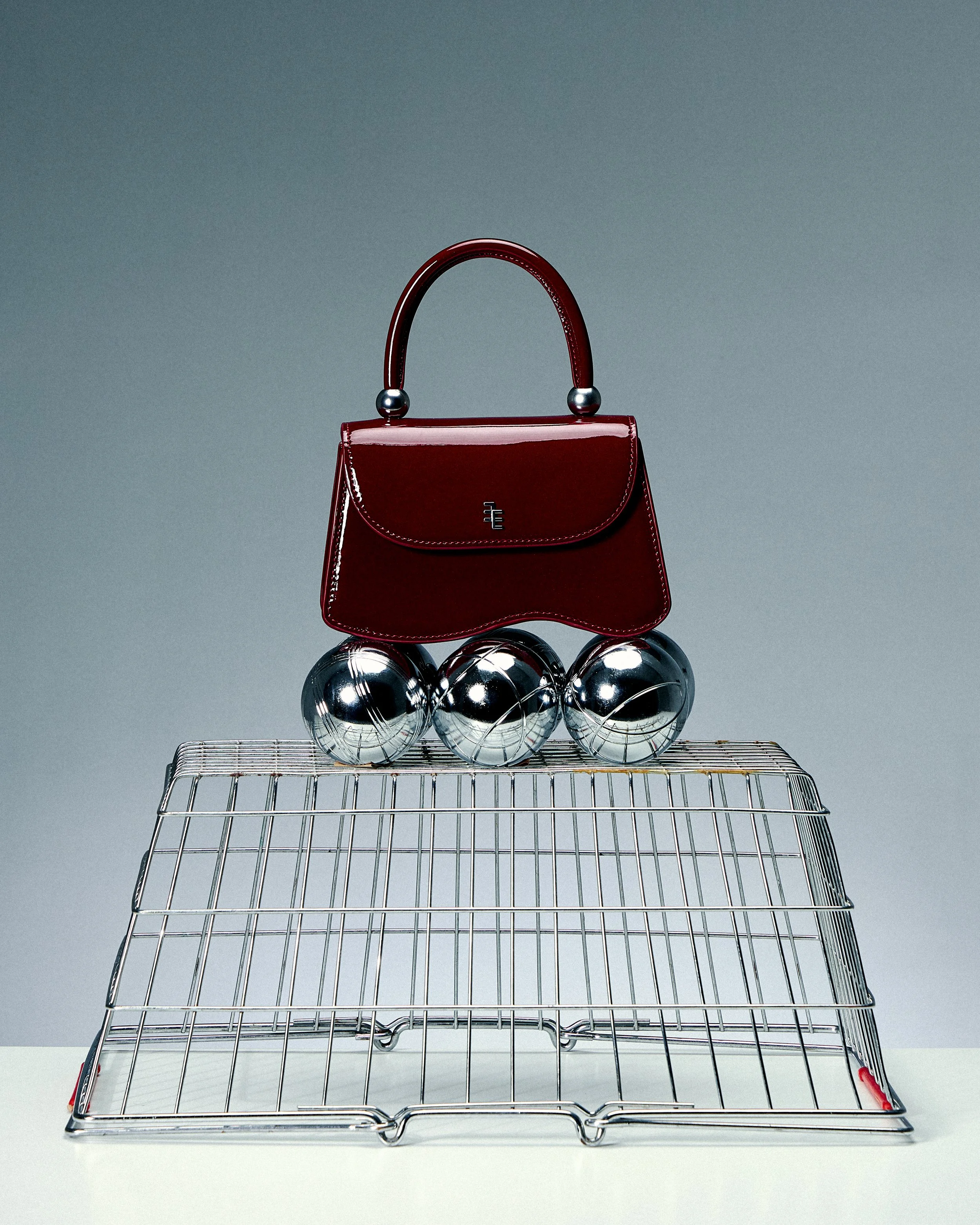 A red handbag placed on chrome balls on a wire rack with a gray background.