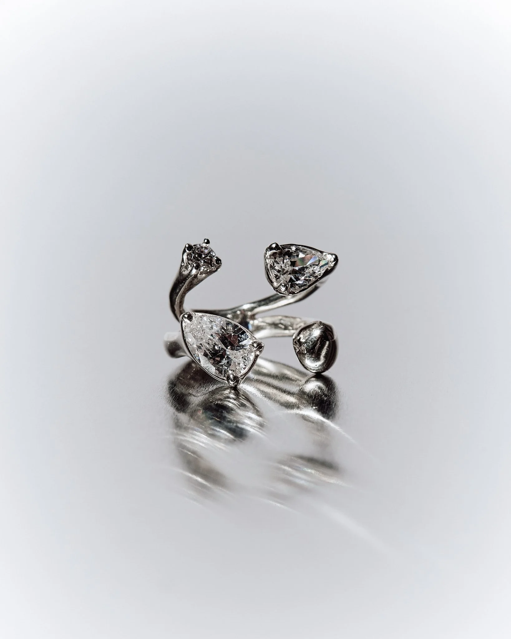 Silver ring with three large clear gemstones arranged in a floral pattern on a reflective surface