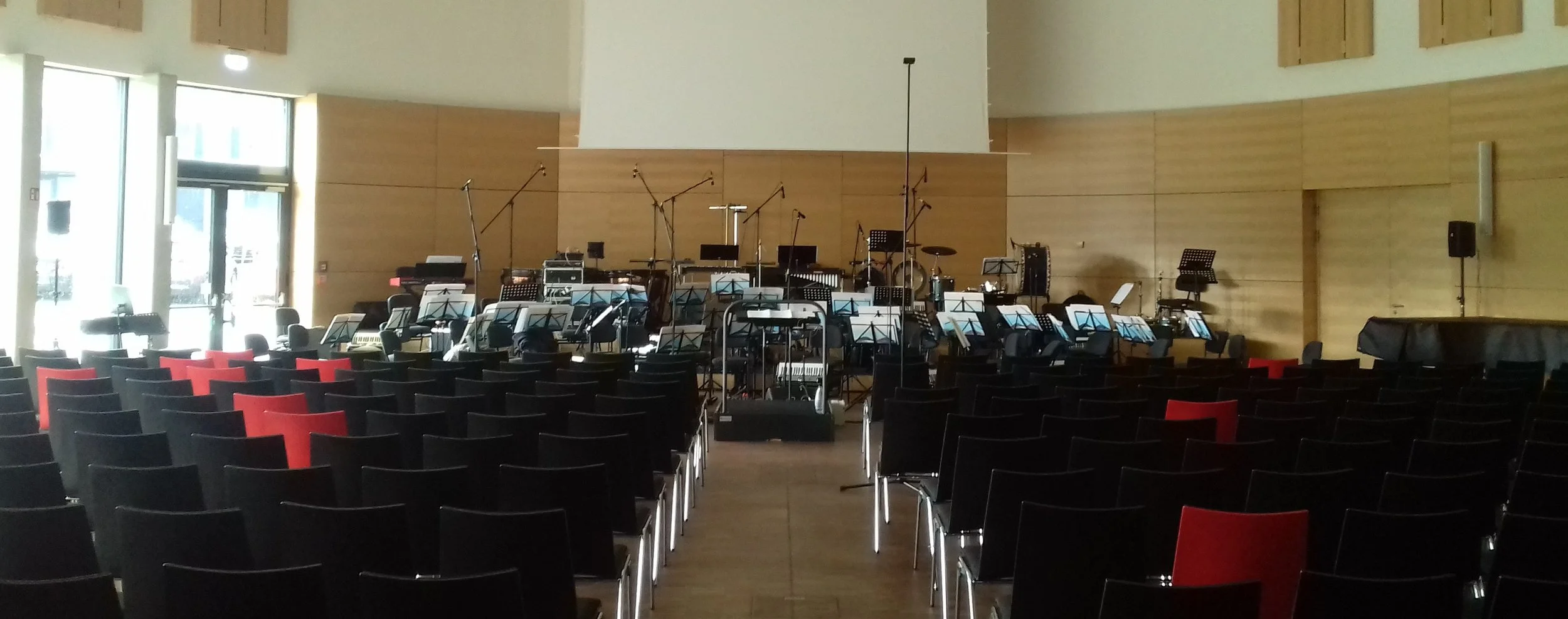 Leerer Veranstaltungs- oder Konzertsaal mit Sitzreihen, einer Bühne, auf der Musikinstrumente und Mikrofone für eine Orchester- oder Musikperformance vorbereitet sind.