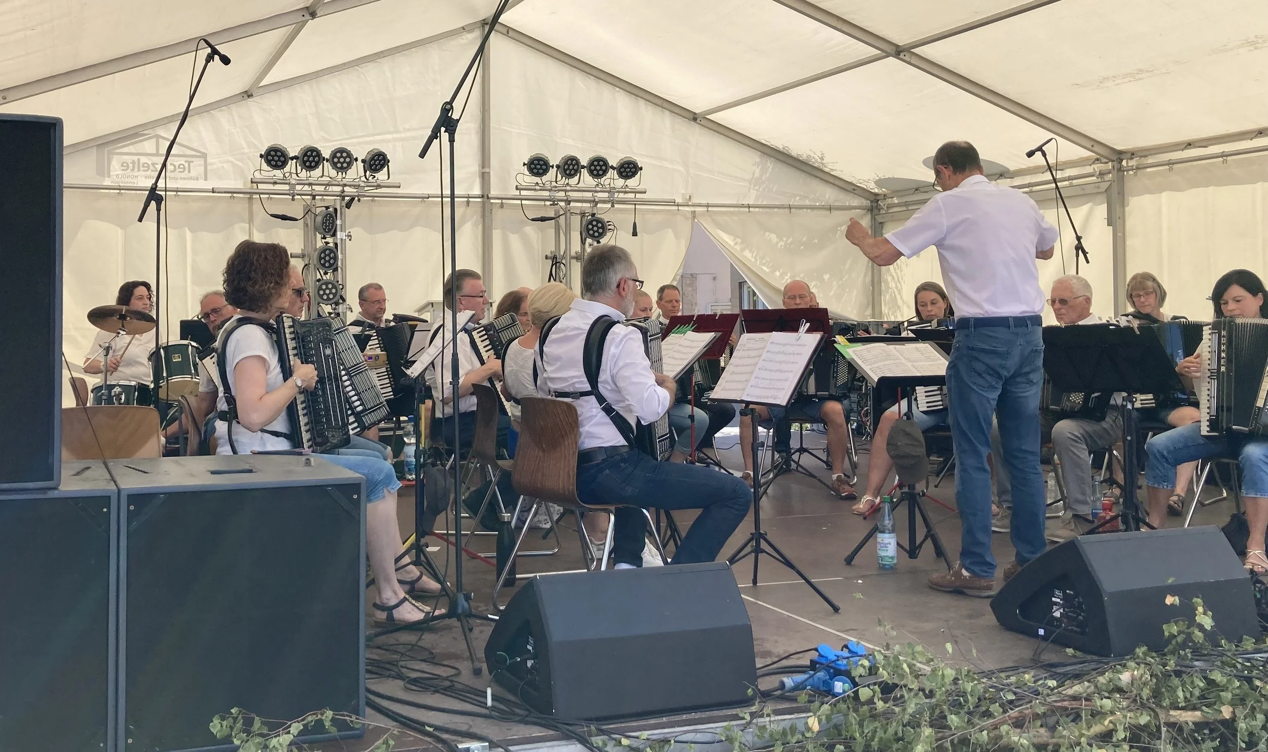 Ein Orchester unter einem großen weißen Zelt, das von einem Dirigenten auf einem Podest geleitet wird.