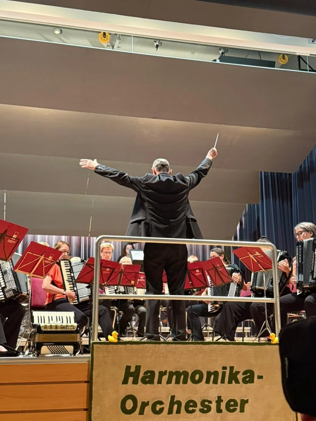 Ein Orchester mit Musikern, die Akkordeon spielen, geleitet von einem Dirigenten auf der Bühne.