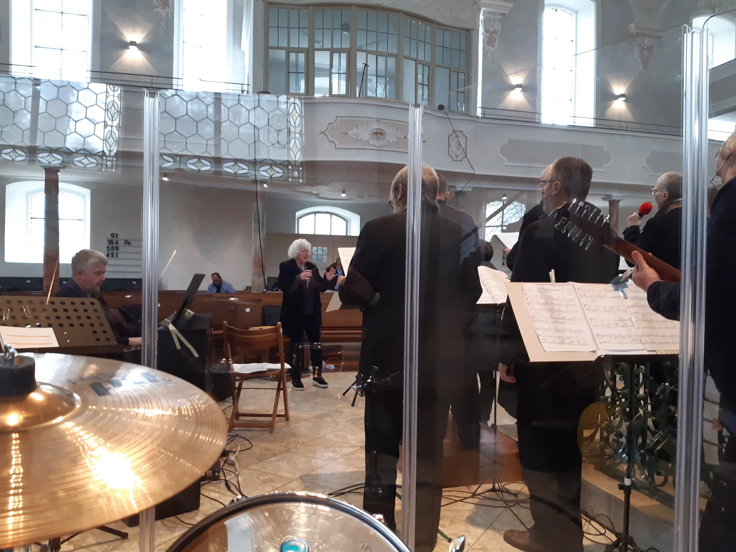 Musiker spielen in einem Saal, im Hintergrund singen Frauen, im Vordergrund ein Schlagzeug und ein Gitarrist.