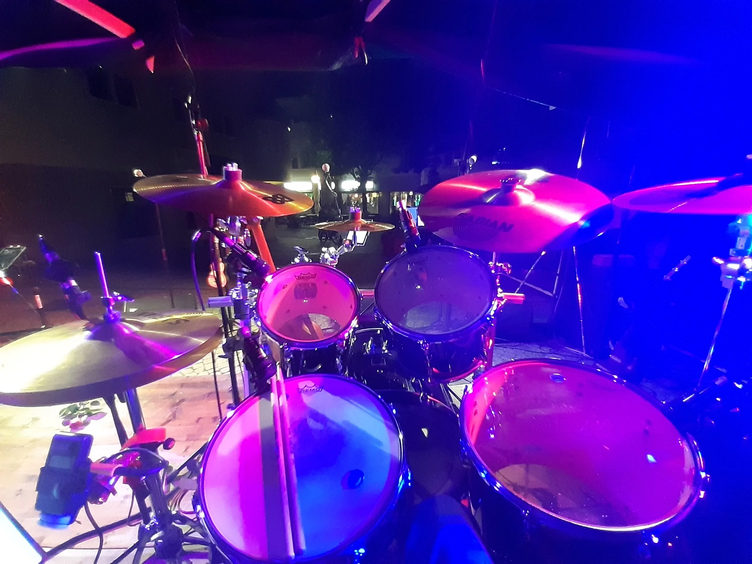 Trommelset mit leuchtenden Drums auf einer Bühne mit bunten Lichtern bei Nacht.