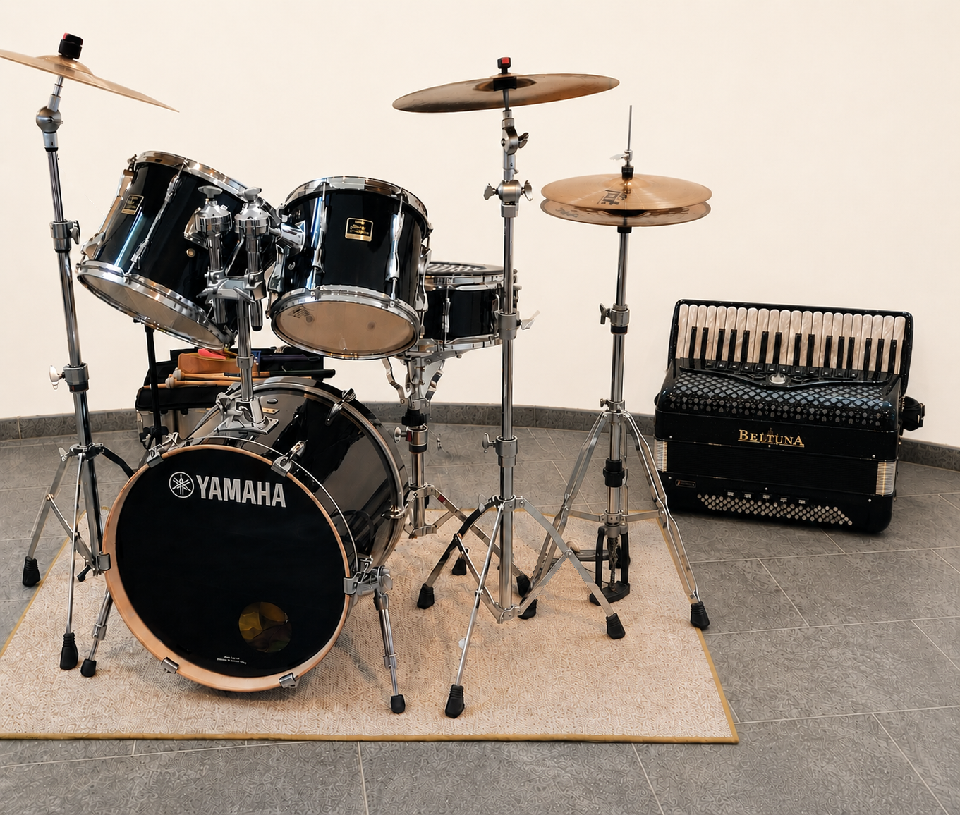 Ein Schlagzeug-Set mit Yamaha-Branding, bestehend aus einer Bassdrum, Toms, Cymbals und Becken, auf einem Teppich vor einer weißen Wand. Daneben steht ein Akkordeon leicht im Hintergrund.
