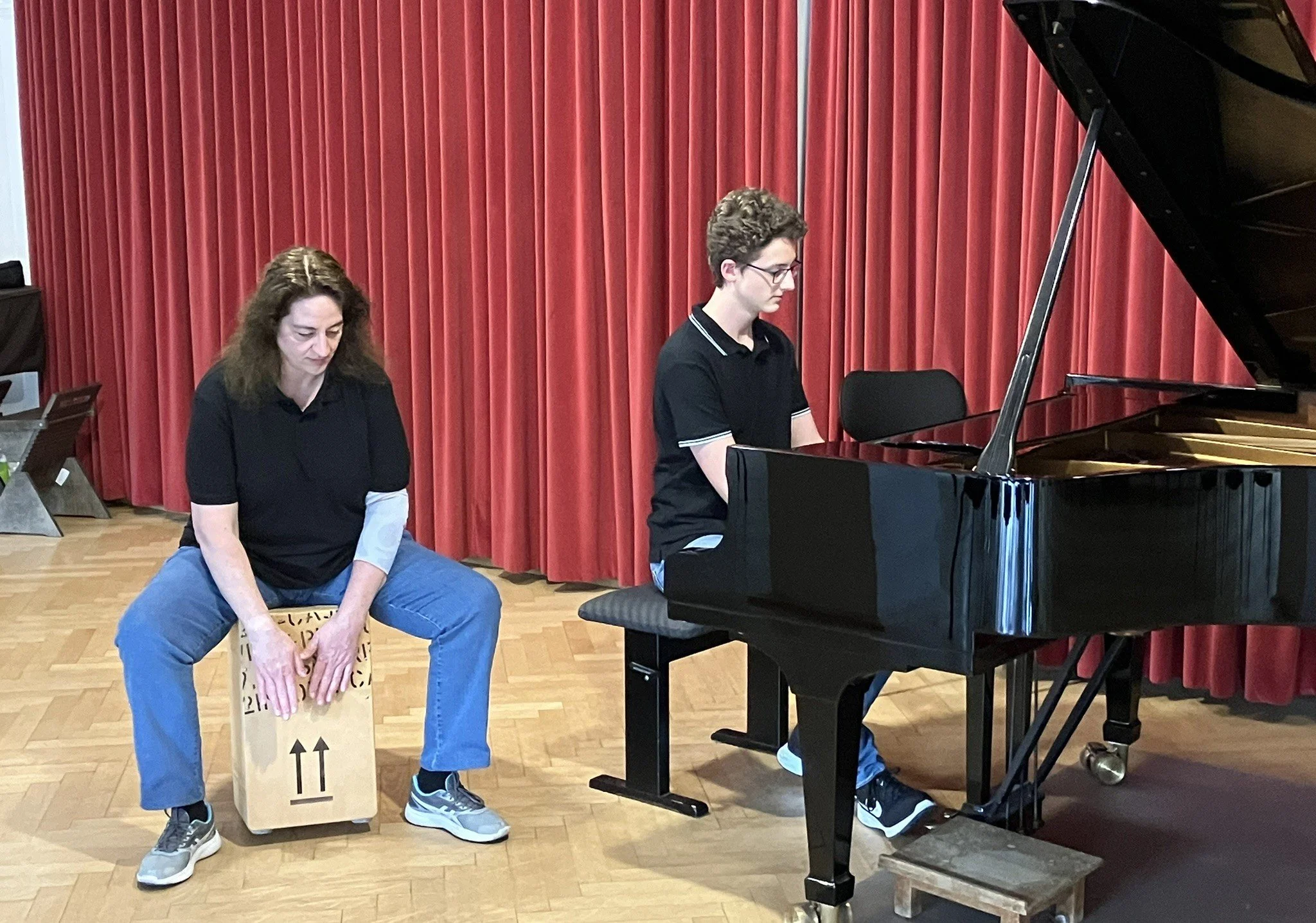 Ein Mann spielt Klavier, während eine Frau auf einer Kiste sitzt und eine Trommel spielt.