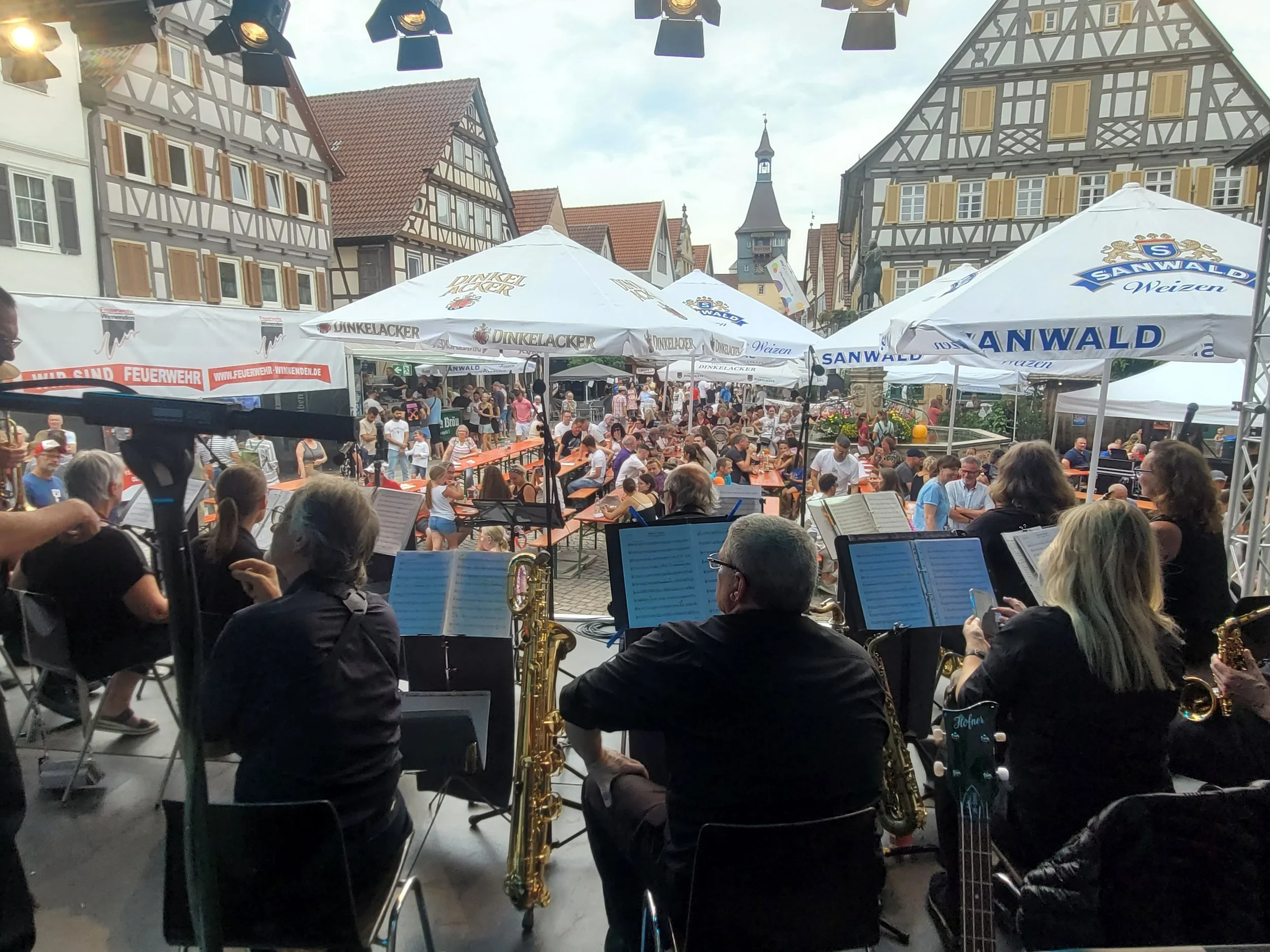 Musiker mit Saxofon und anderen Instrumenten, die in einer Volksfest- oder Konzertveranstaltung spielen, im Hintergrund historische Fachwerkhäuser in einer Stadtmitte mit vielen Zuschauern.