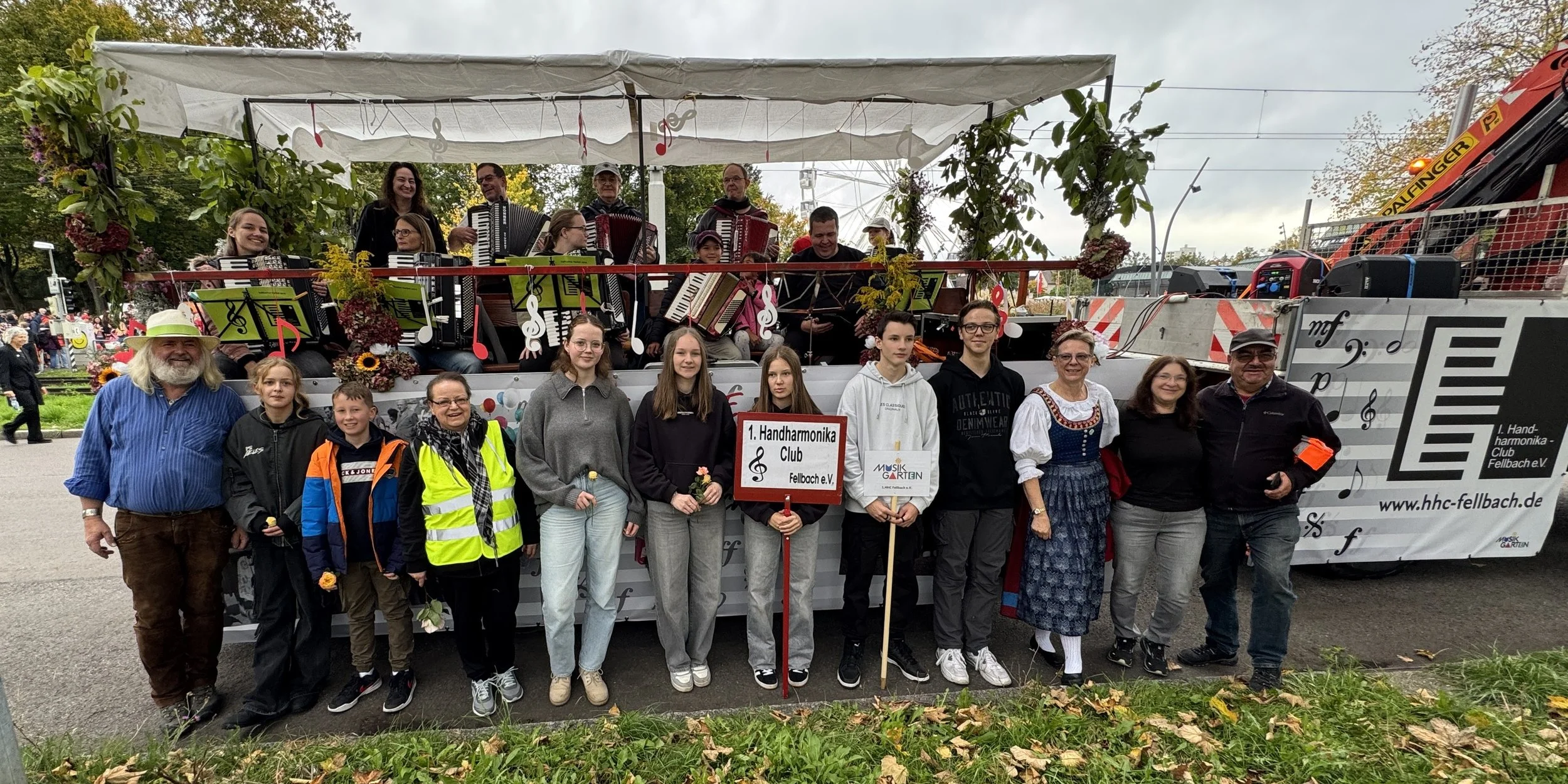 Gruppe von Menschen vor einem Musik-Umzugwagen mit einem Orchester, darunter Kinder, Jugendliche und Erwachsene, bei einem Fest oder Umzug in Fellbach, Deutschland.