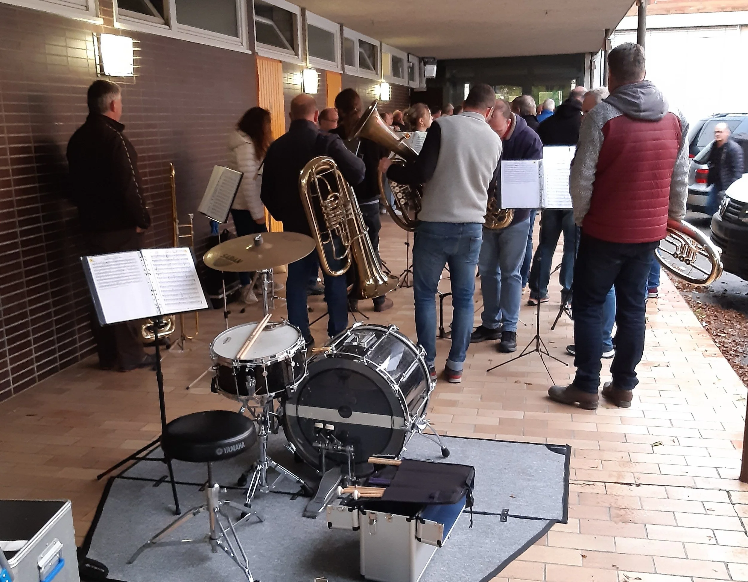 Menschen machen Musik im Freien, einige spielen Instrumente wie Tuba, Trompete und Schlagzeug, während andere zuhören.
